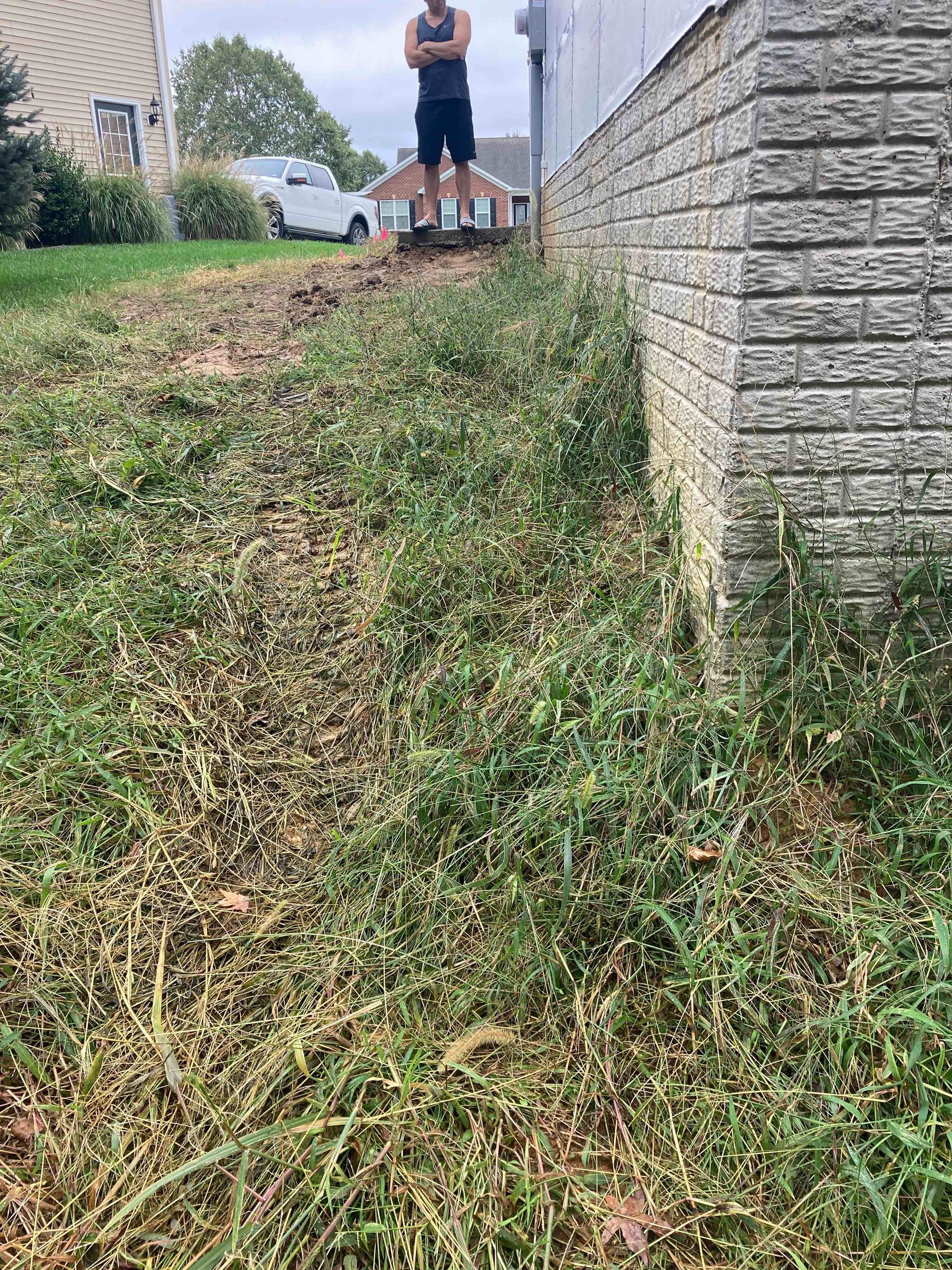 Person standing on a grassy slope beside a stone wall, with houses in the background.