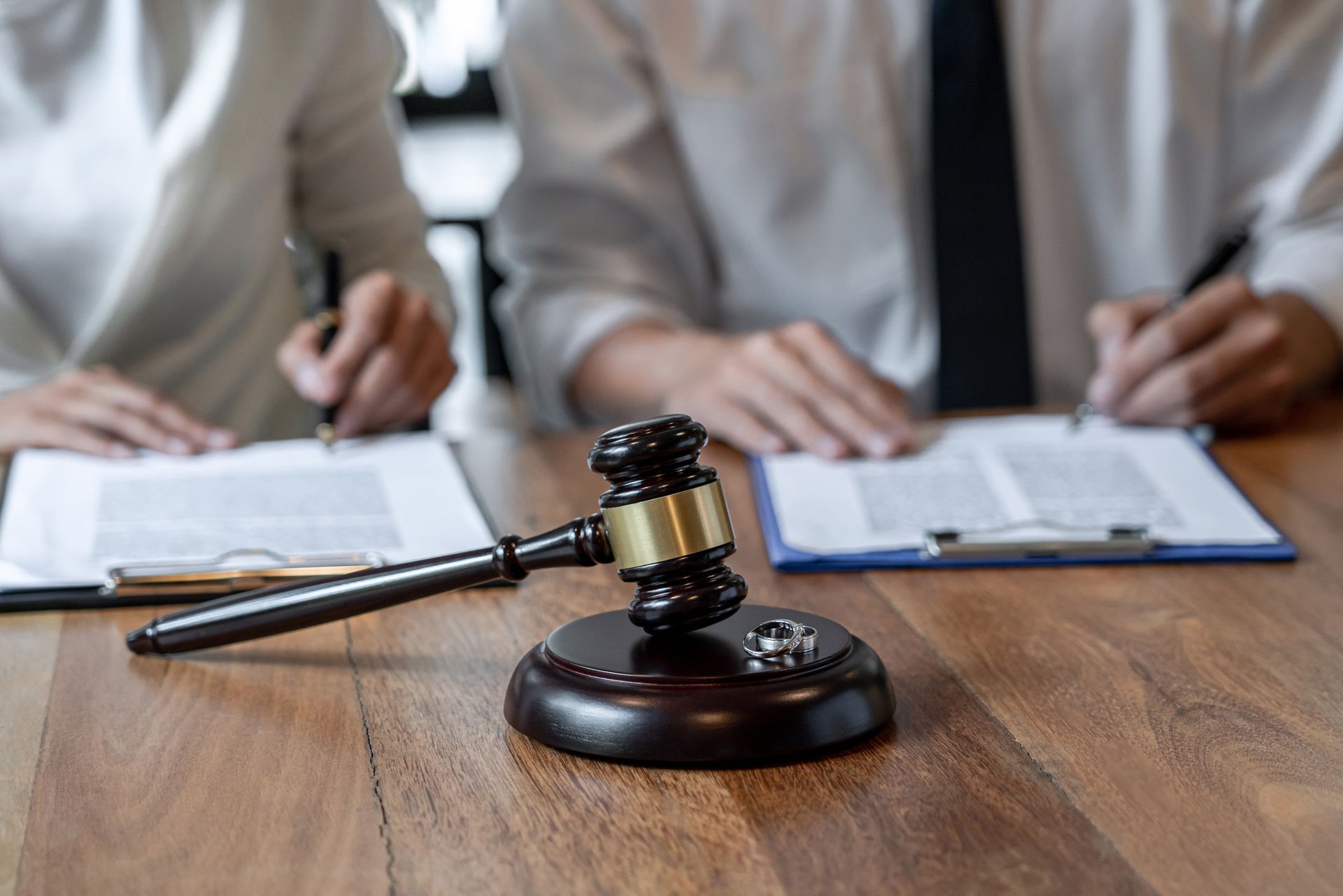 A pair of spouses sit in front of a table with a gavel on top of it, with two wedding rings.