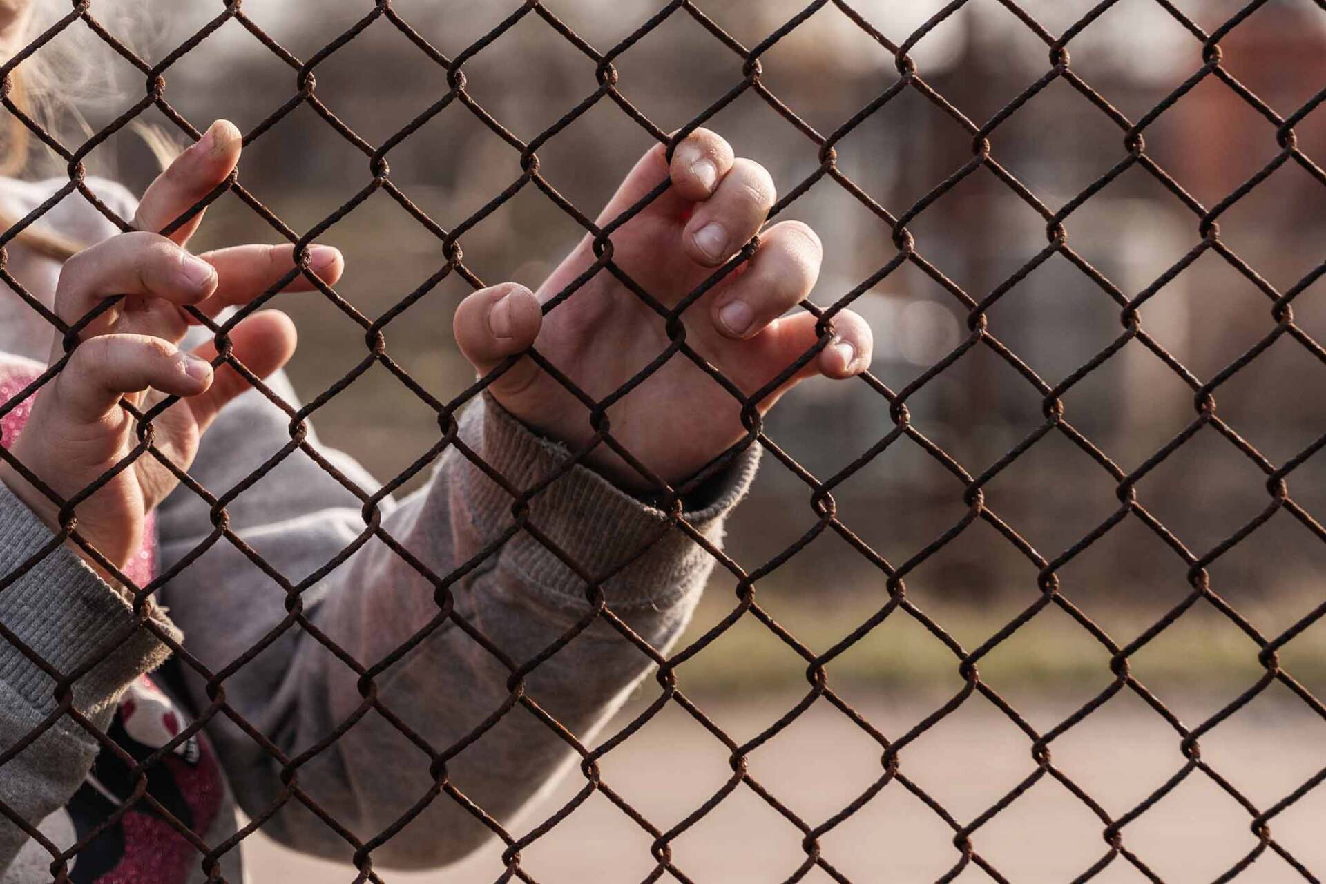 A person is holding onto a chain link fence with their hands.