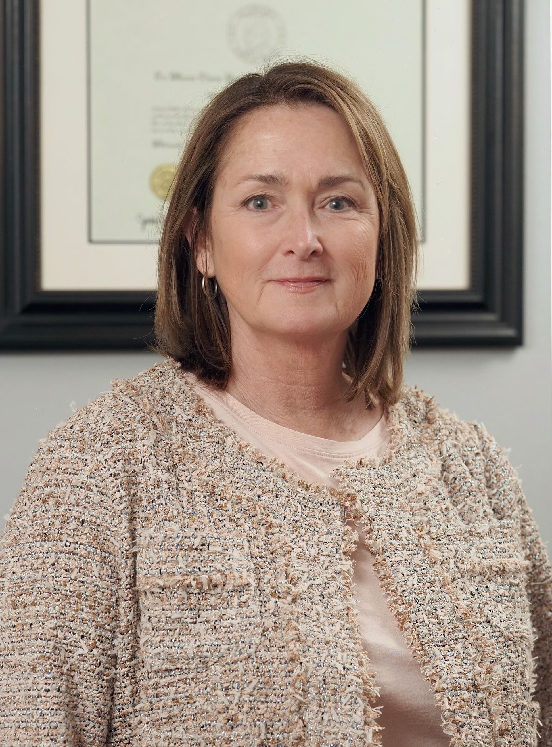 A woman in a sweater is standing in front of a framed picture.
