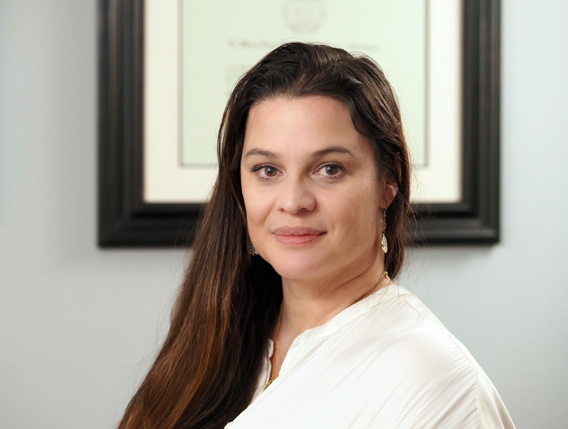A woman in a white shirt is standing in front of a framed picture.