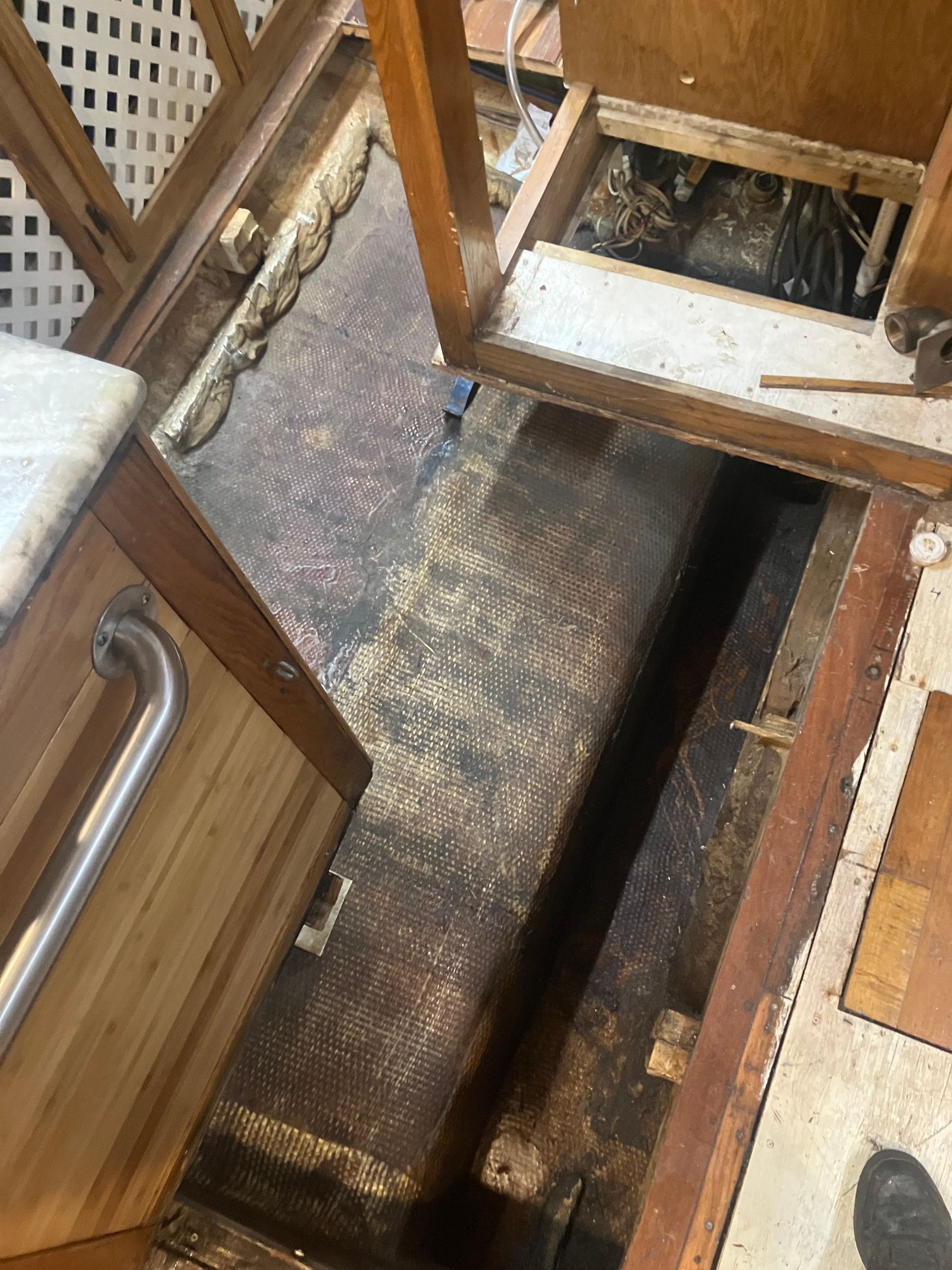 Interior of a boat, showing open floorboards, exposed wiring, and a dark, textured surface.