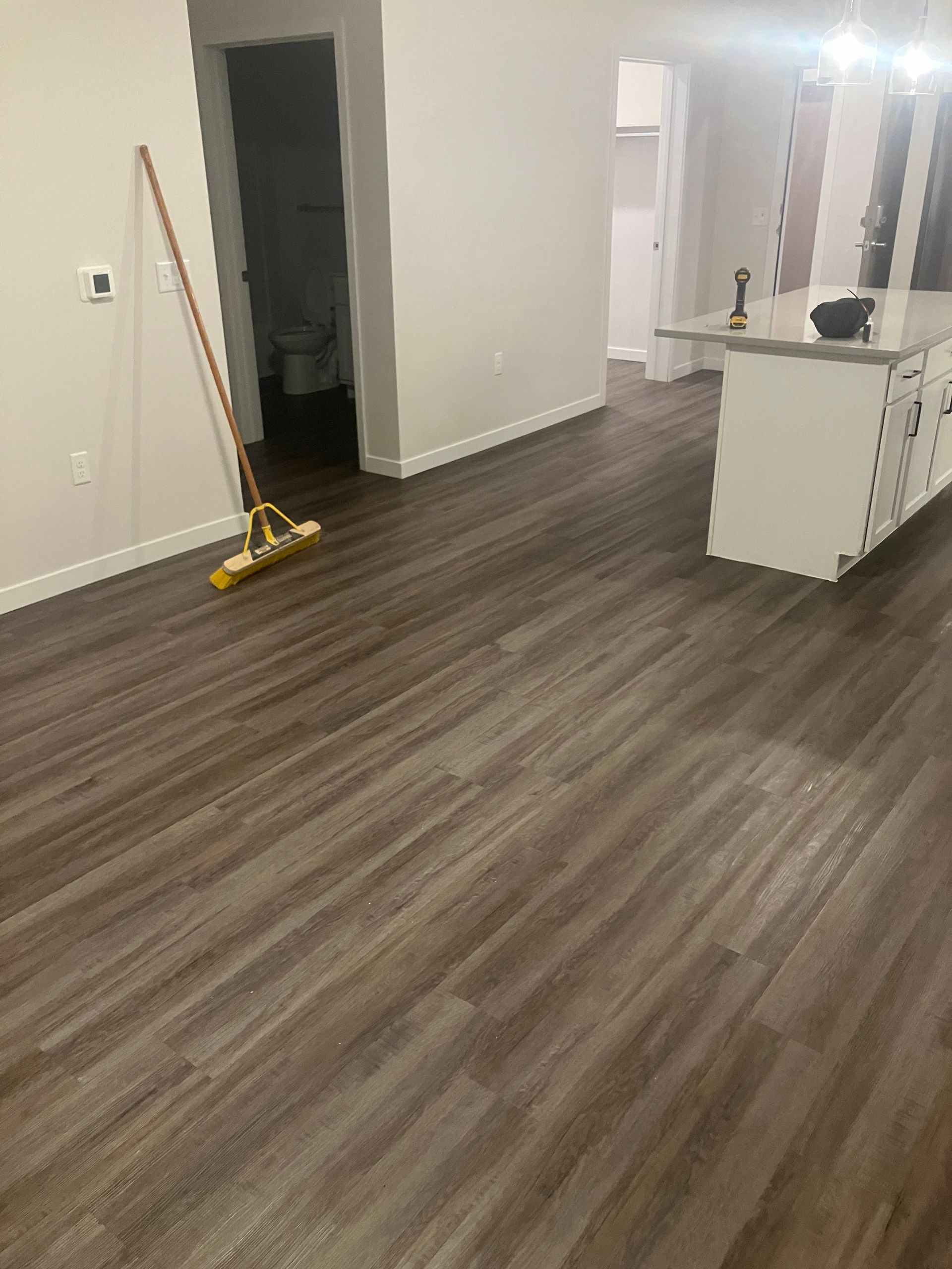 A room with wood-look flooring, white cabinets, and a broom leaning against the wall.