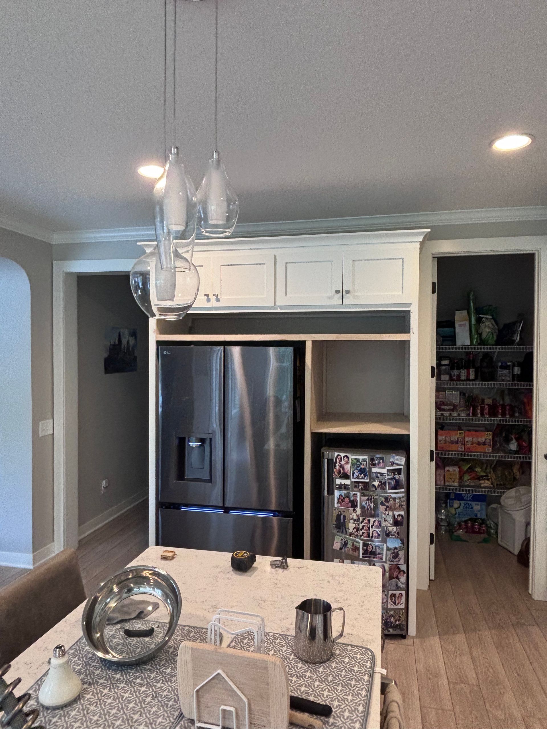 Kitchen with refrigerator, built-in storage, pantry, and pendant lights over a countertop island.