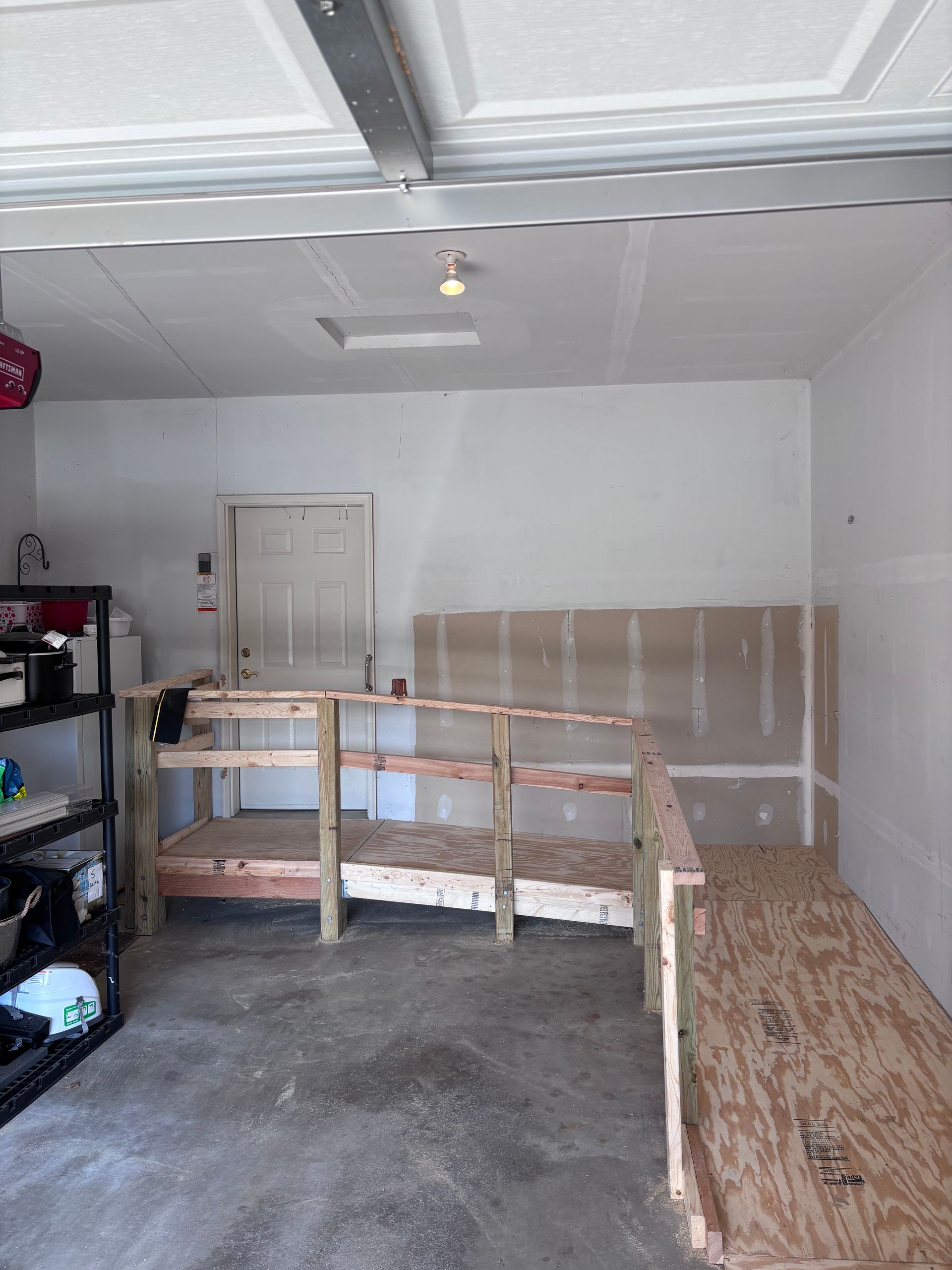 Garage interior with a wooden ramp and shelving, plywood leaning against the wall.