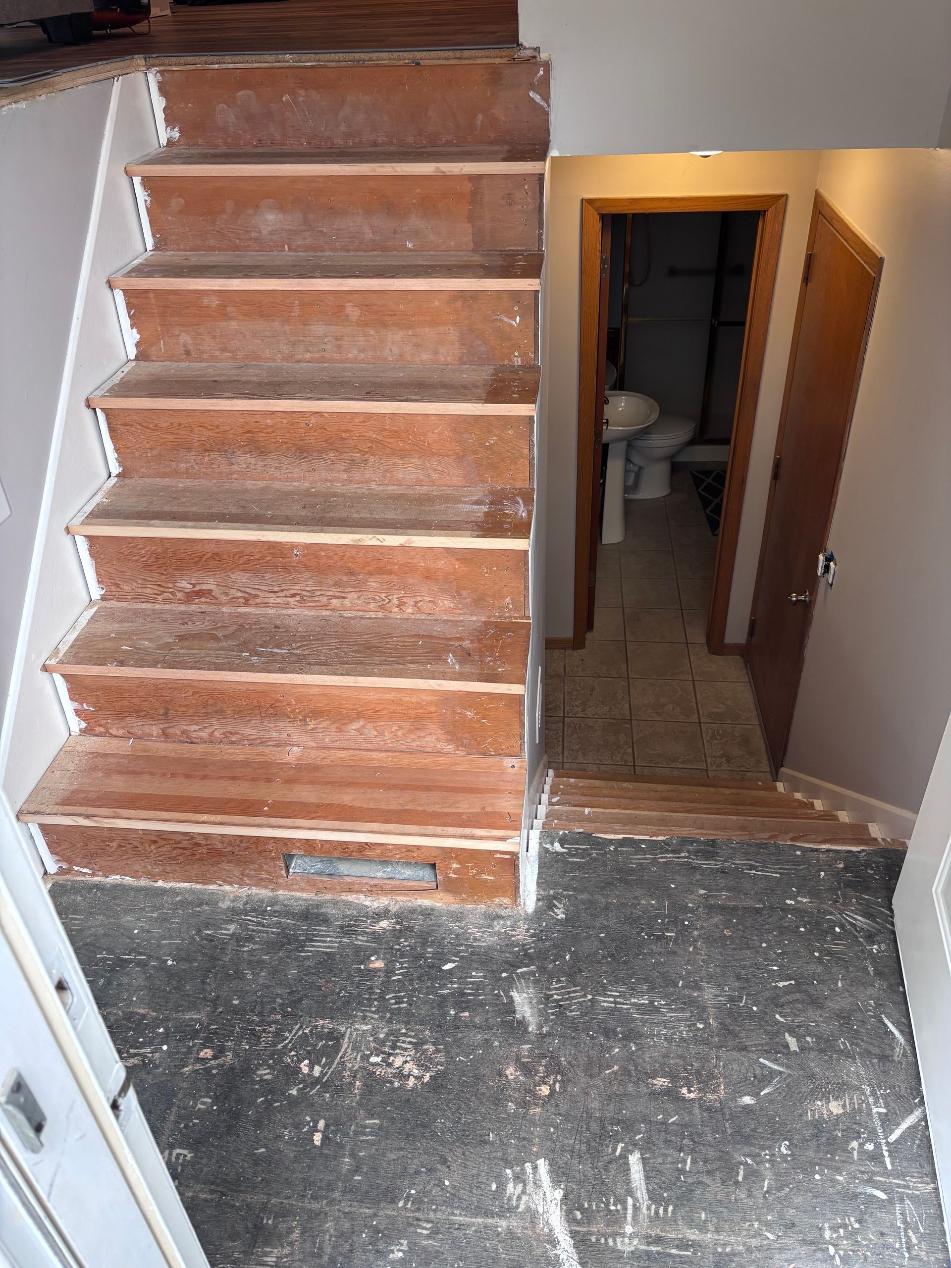 Staircase with wooden steps leading down to a landing and a bathroom with a toilet and door.