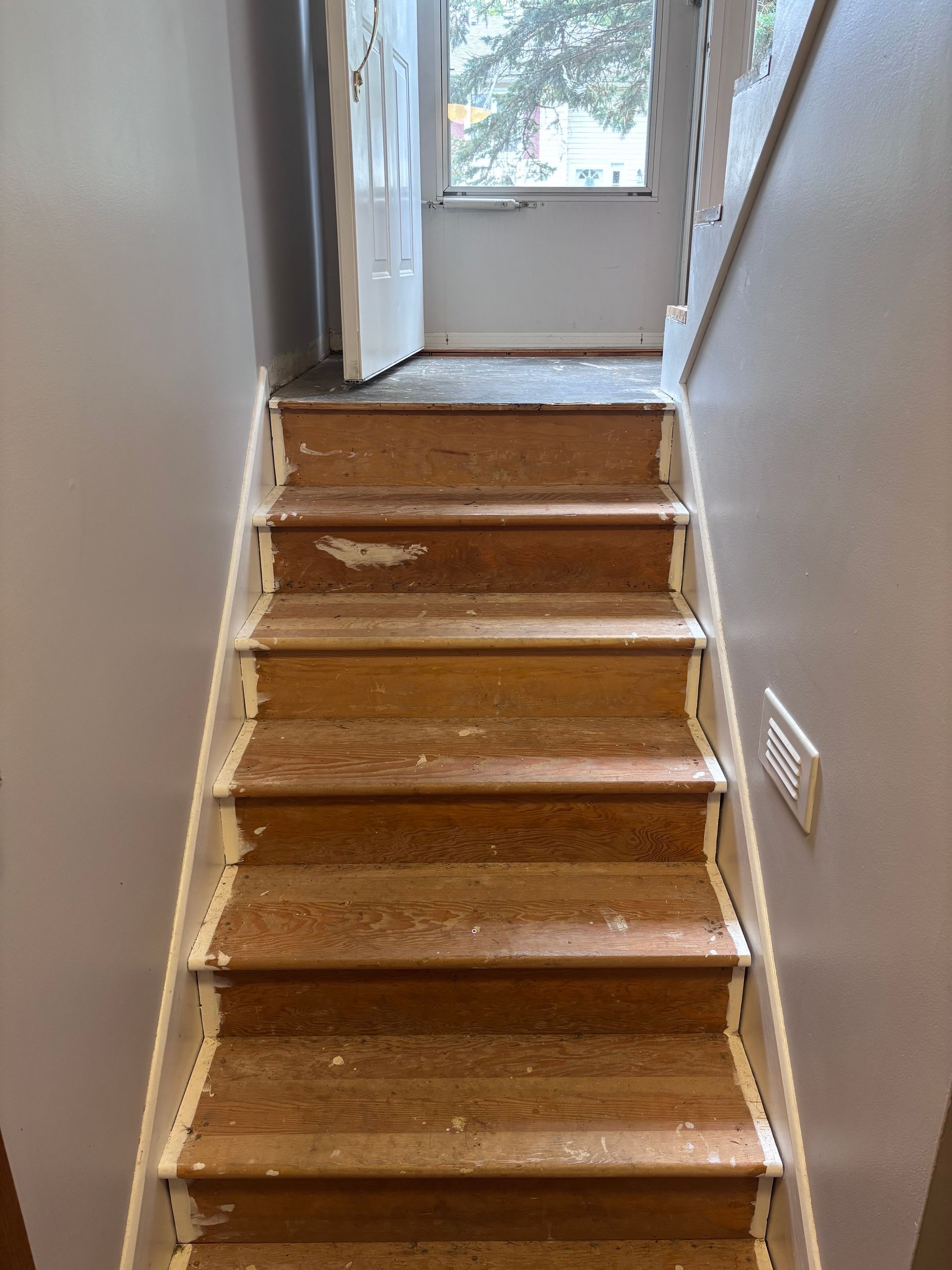 Staircase with worn wooden steps, white trim, and a door at the top. Grey walls surround.