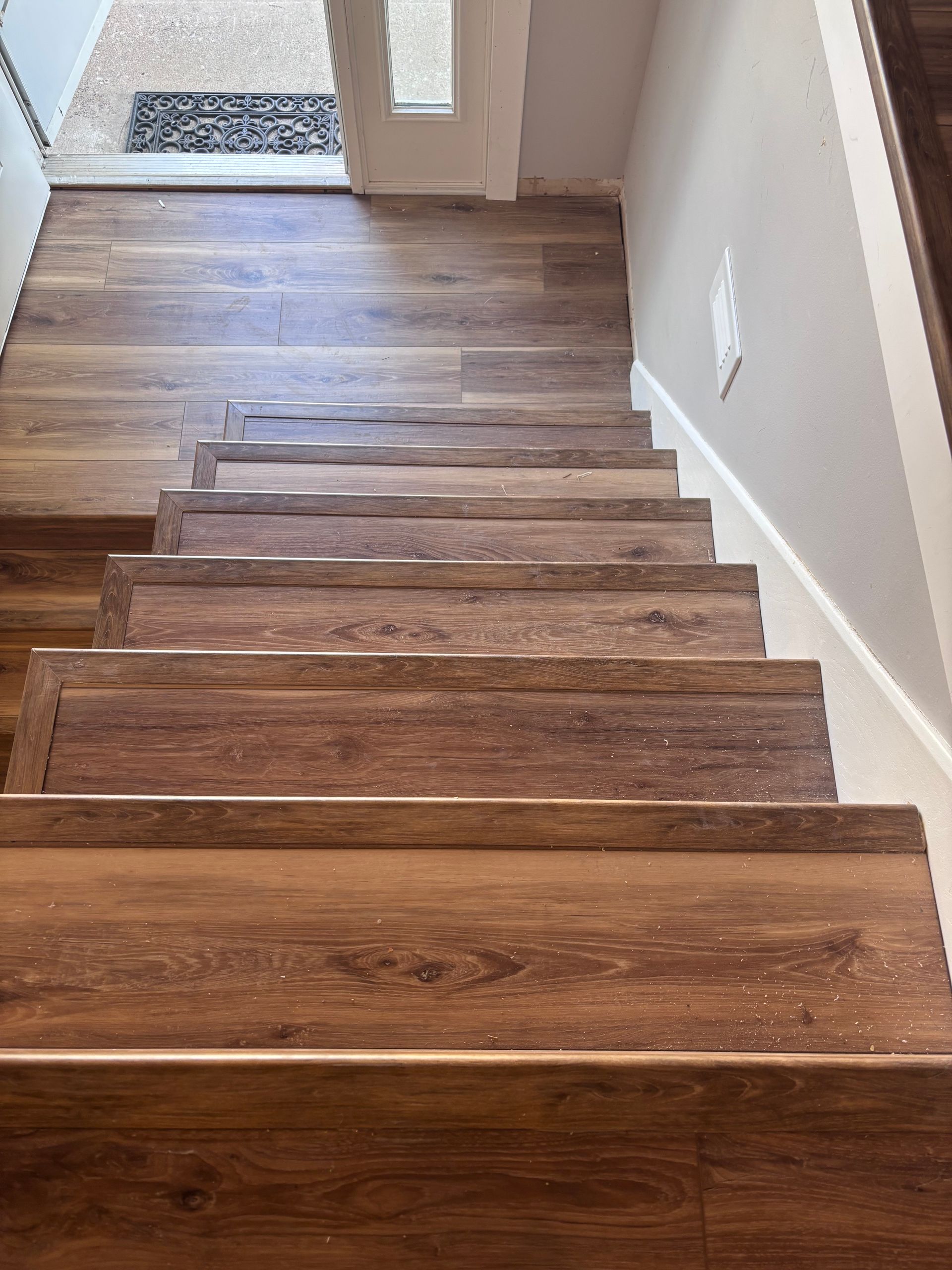 Wooden stairs leading down, lined with a dark wood-look flooring, with a rug at the top.