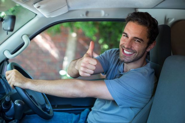 A person smiling and giving a thumbs-up while driving a car.