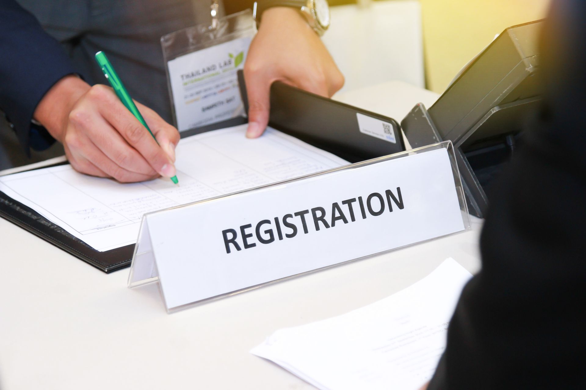 A person writes on a registration form at a desk with a white 