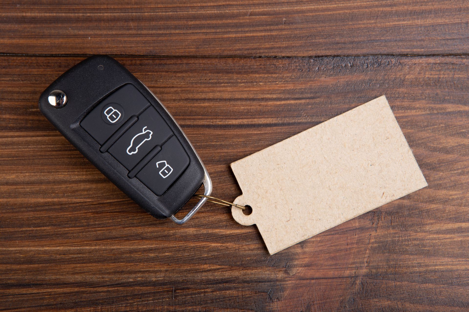 A black car key fob with a blank brown paper tag resting on a dark wood surface.