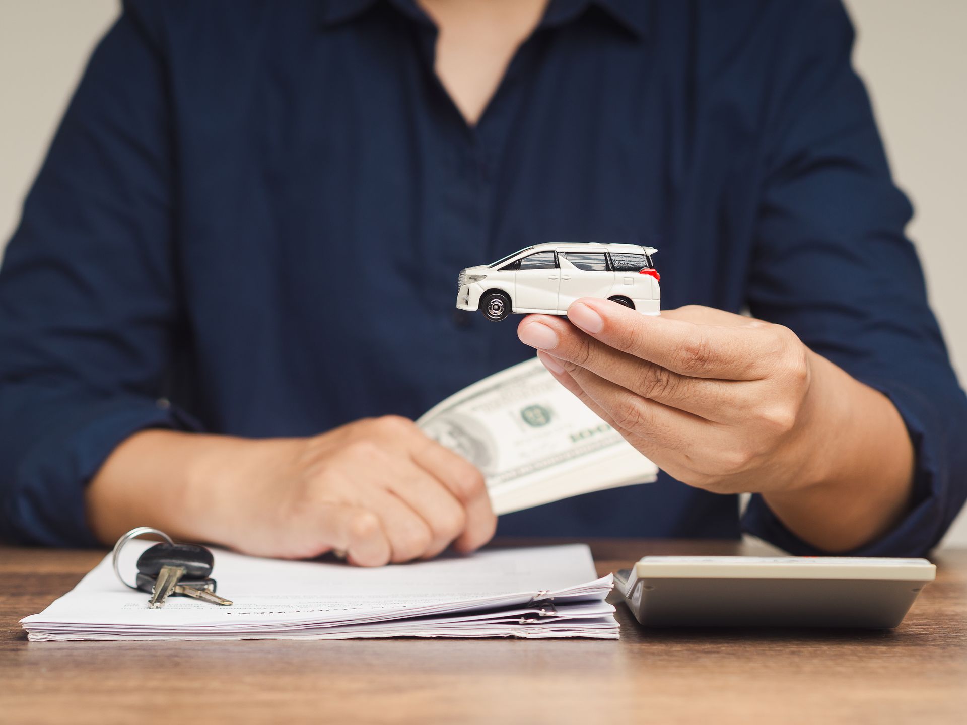 Person counts cash and holds a credit card over paperwork beside a calculator at a desk.