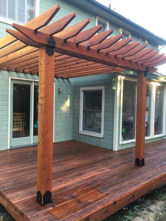 Wooden pergola over a deck with a house in the background. Brown wood structure.
