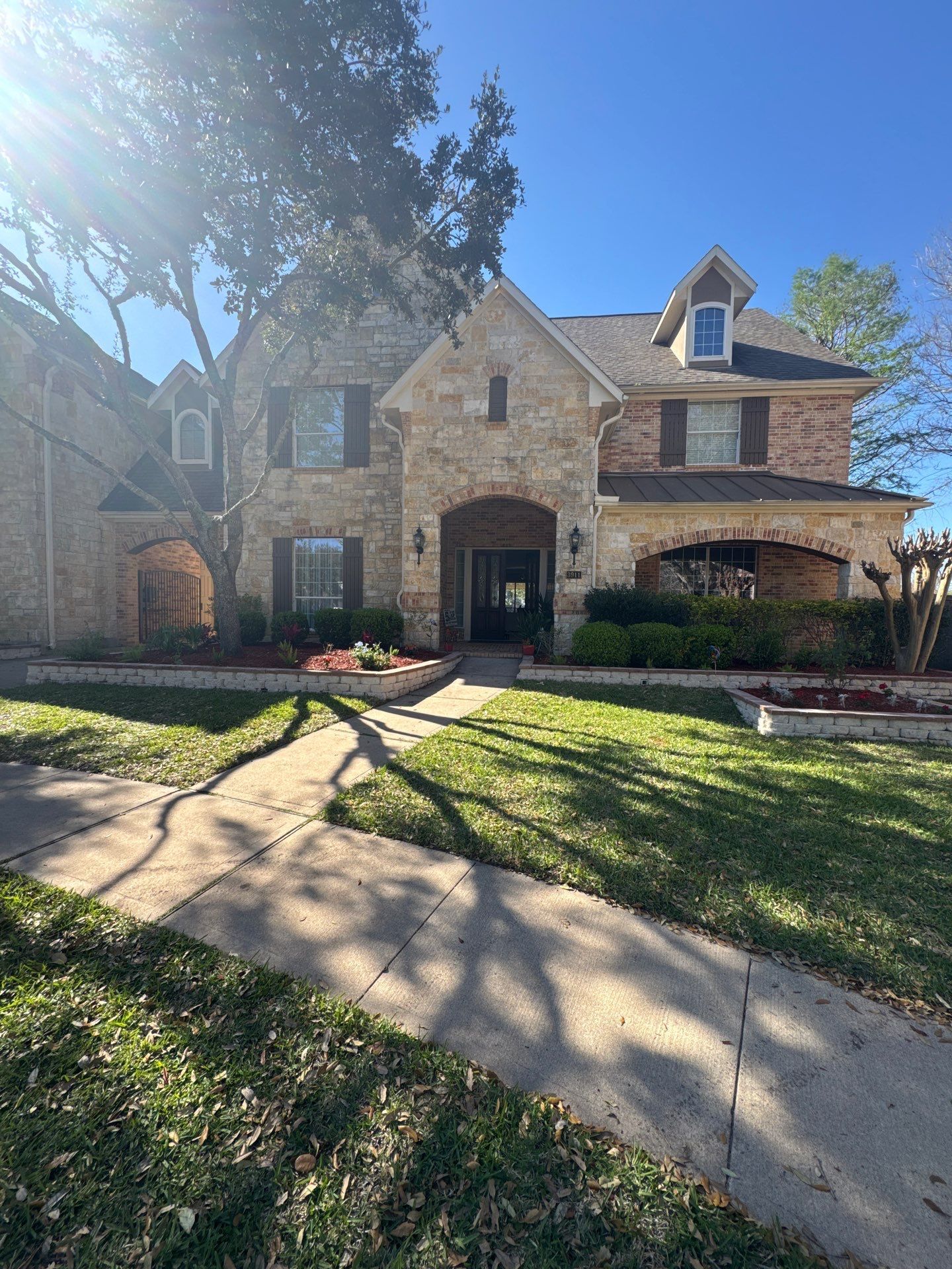 Two-story brick house with stone accents, arched entryway, and well-manicured lawn on a sunny day.