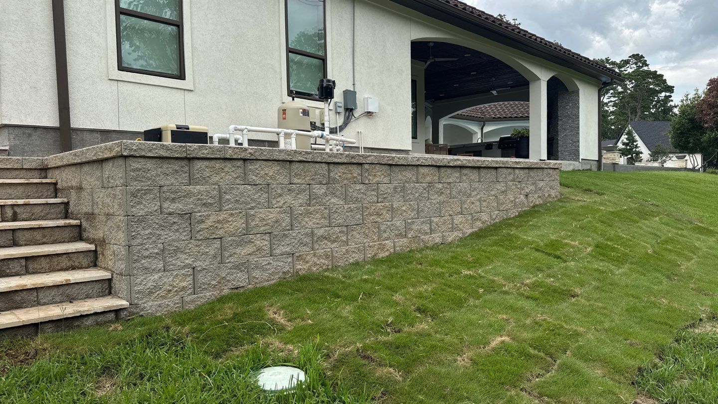 A house with a stone retaining wall and grass lawn. Steps leading up to the patio area.