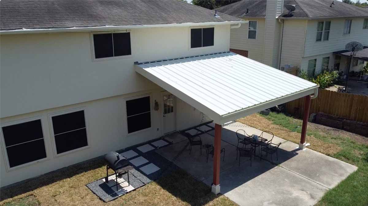White house with a patio roof over outdoor seating, grill, and concrete patio.