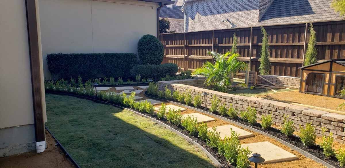 A well-manicured backyard with a pathway, garden beds, stone wall, and wooden fence.