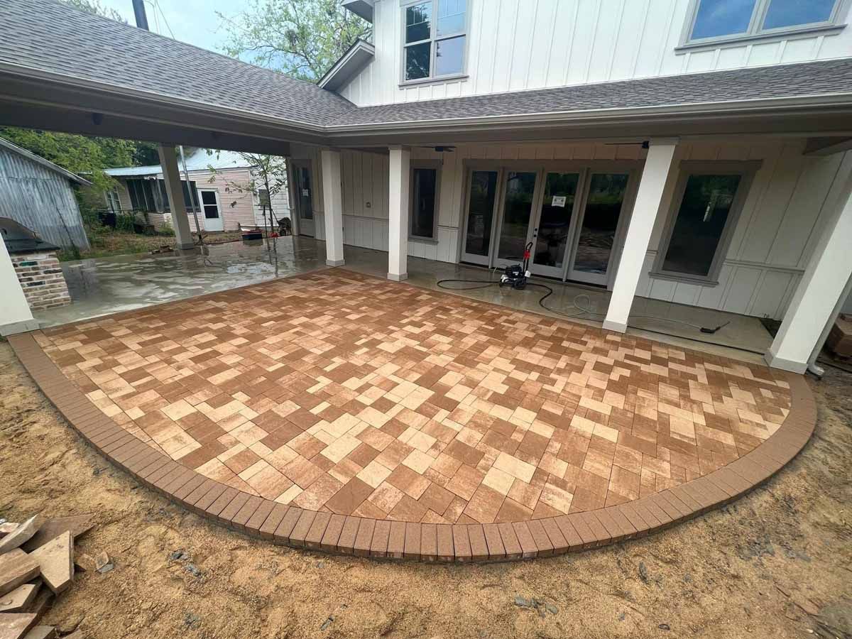 Brick patio under a covered porch, with curved brick border and house in background.