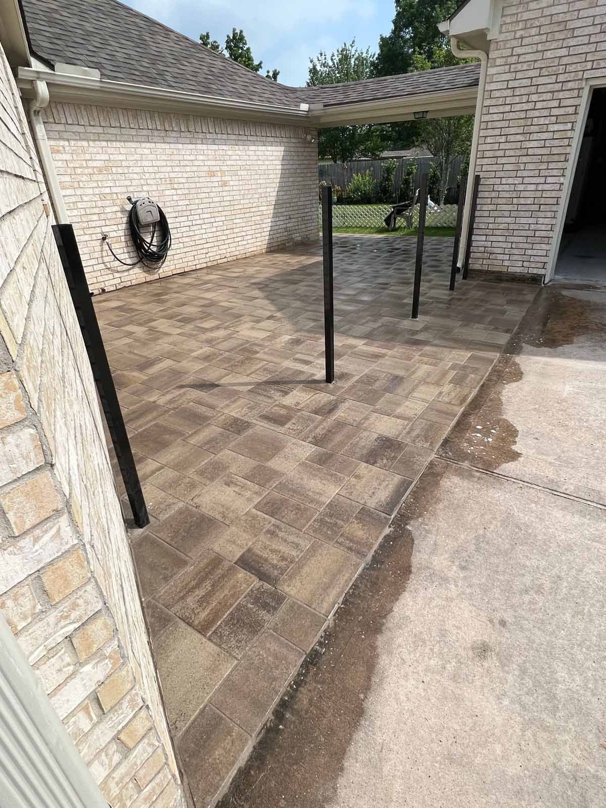 Brick patio with dark pillars, adjacent to a brick house and driveway.