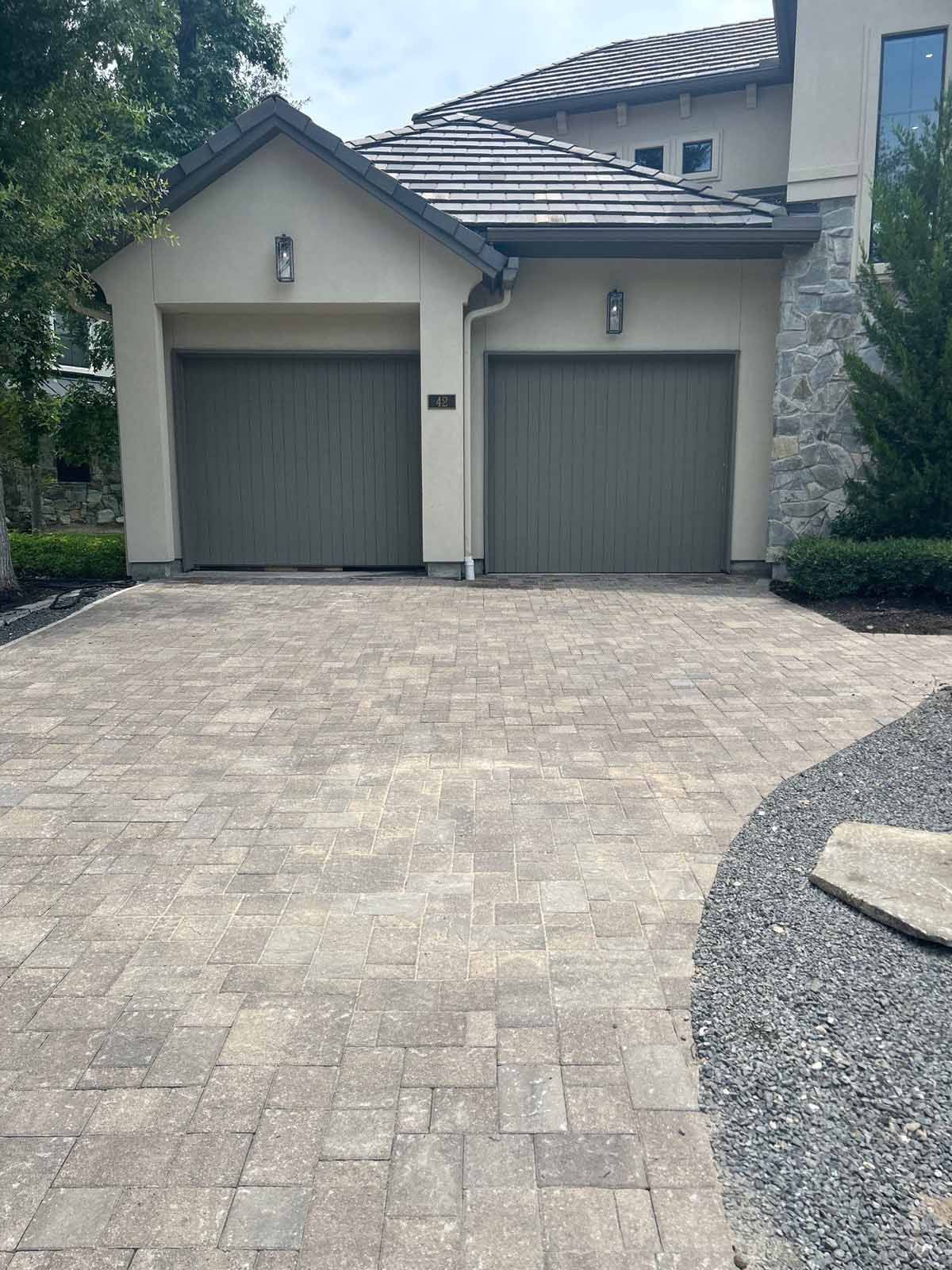 Driveway paved with blocks leading to a two-car garage with green doors.