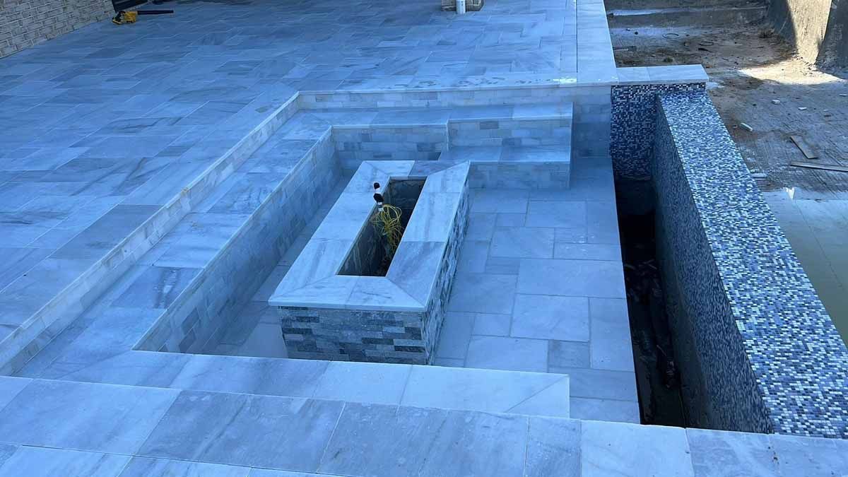 Stone patio with built-in fire pit and adjacent wall; light gray and blue tones, exterior setting.