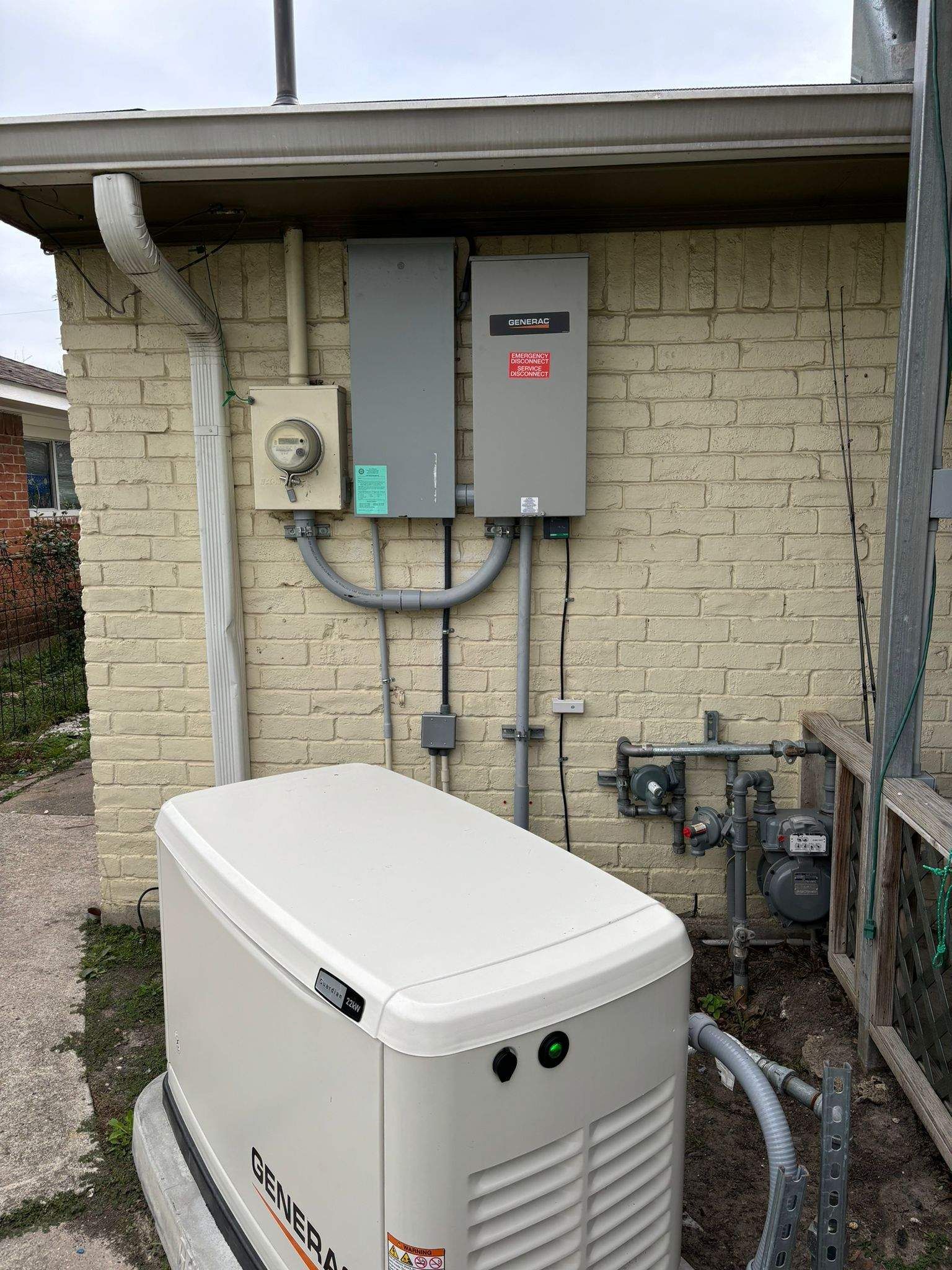 Generator and electrical boxes on a brick wall next to a gas meter.