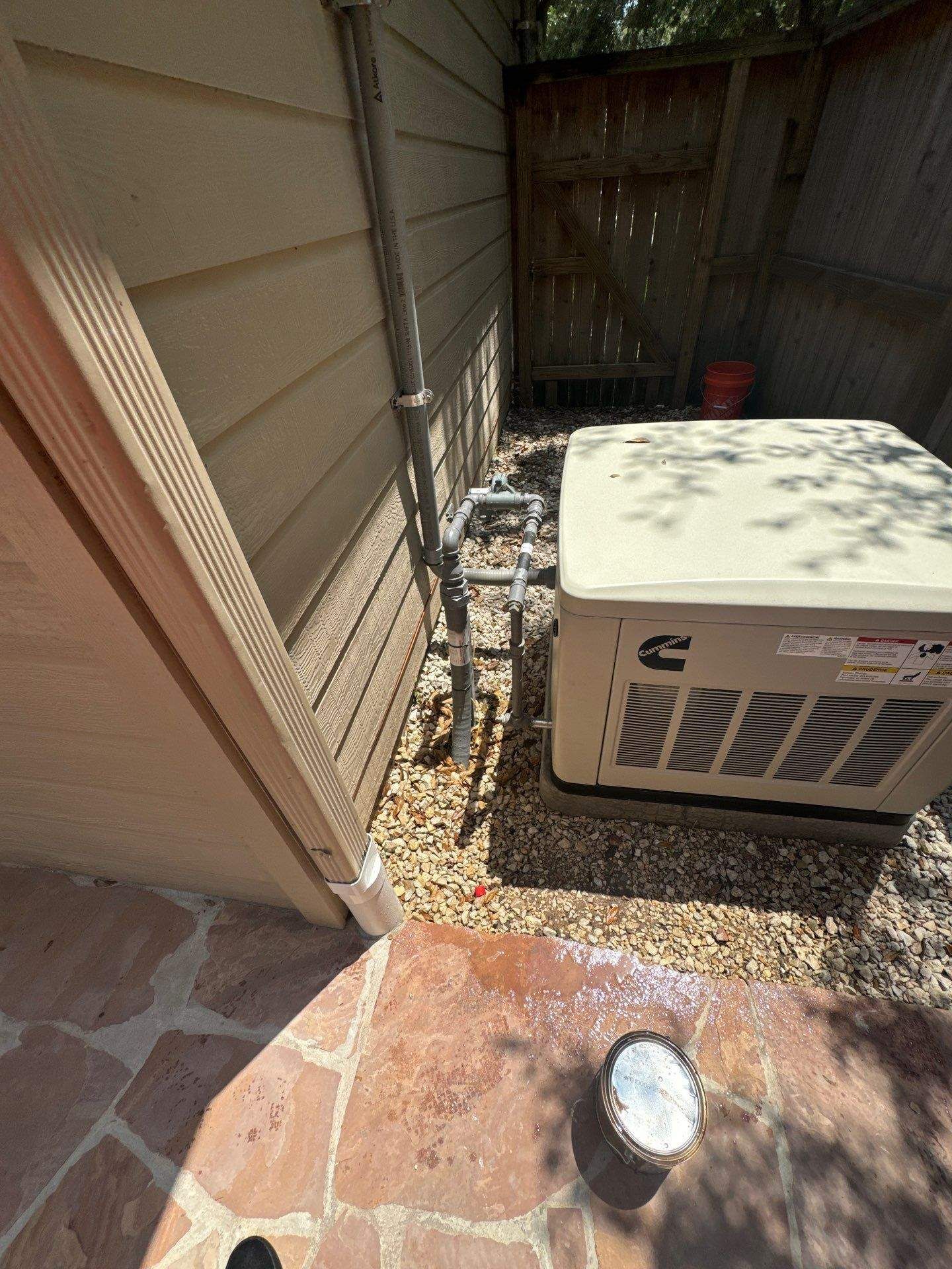 A beige generator beside a building and fence, on gravel. A small amount of spilled white paint on the stone patio.