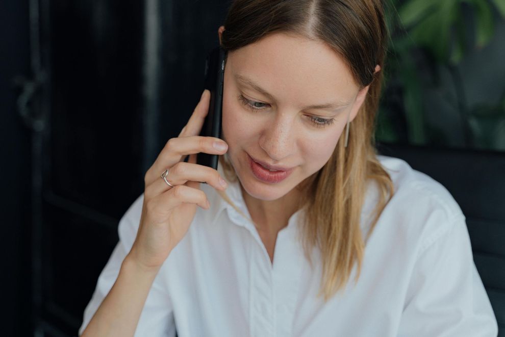 Person in a white shirt talking on a phone, looking down with a focused expression.