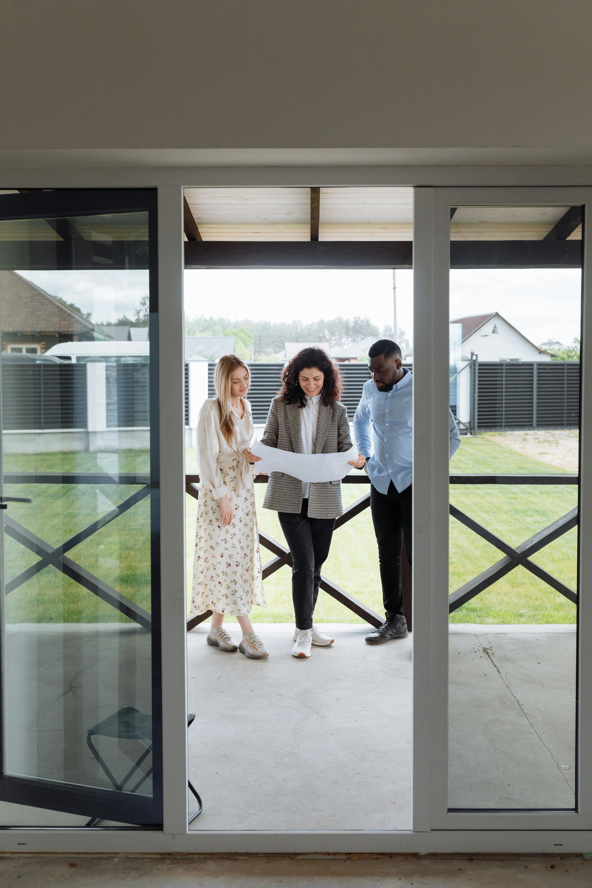 Three people standing in a doorway, holding a large sign outside a house.