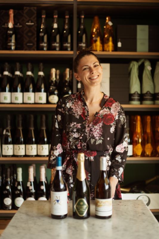 la titolare è in piedi accanto a tre bottiglie di vino su un tavolo.