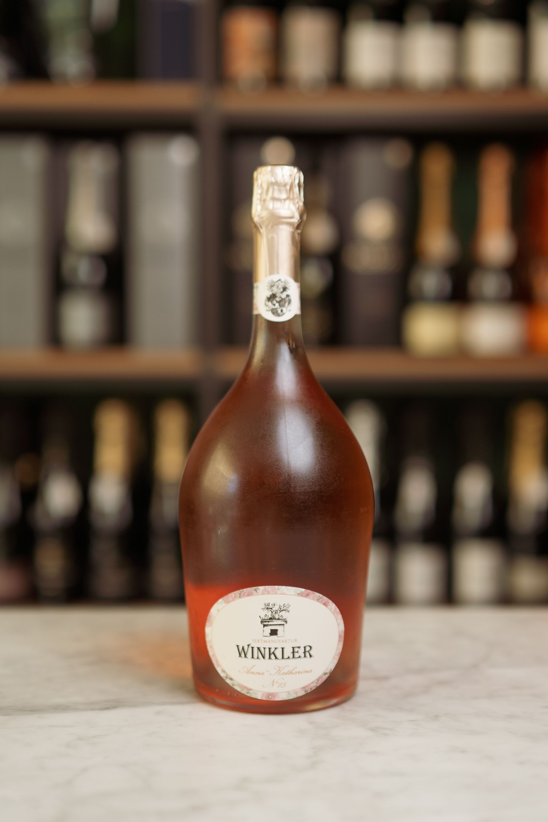 Una bottiglia di vino è appoggiata su un tavolo davanti a uno scaffale.