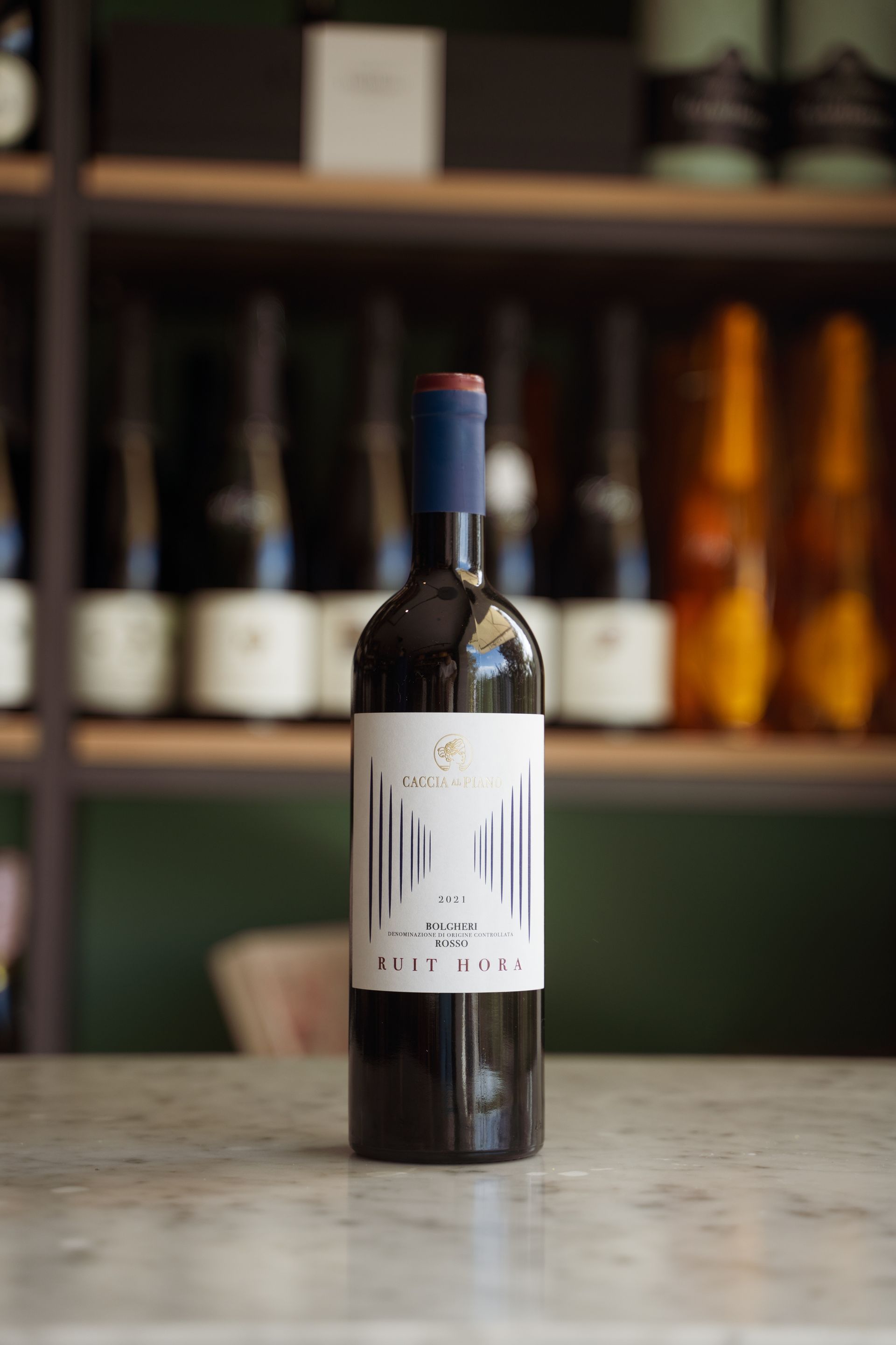 Una bottiglia di vino è appoggiata su un tavolo di fronte a uno scaffale pieno di bottiglie di vino.