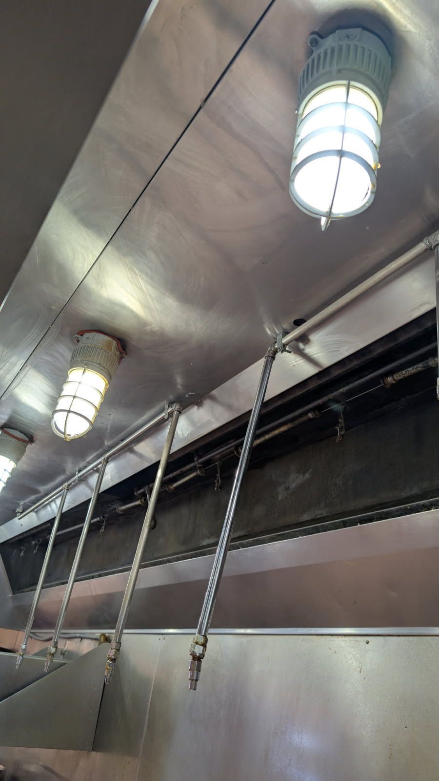 Stainless steel kitchen hood with three caged lights. A silver ladder extends downwards.
