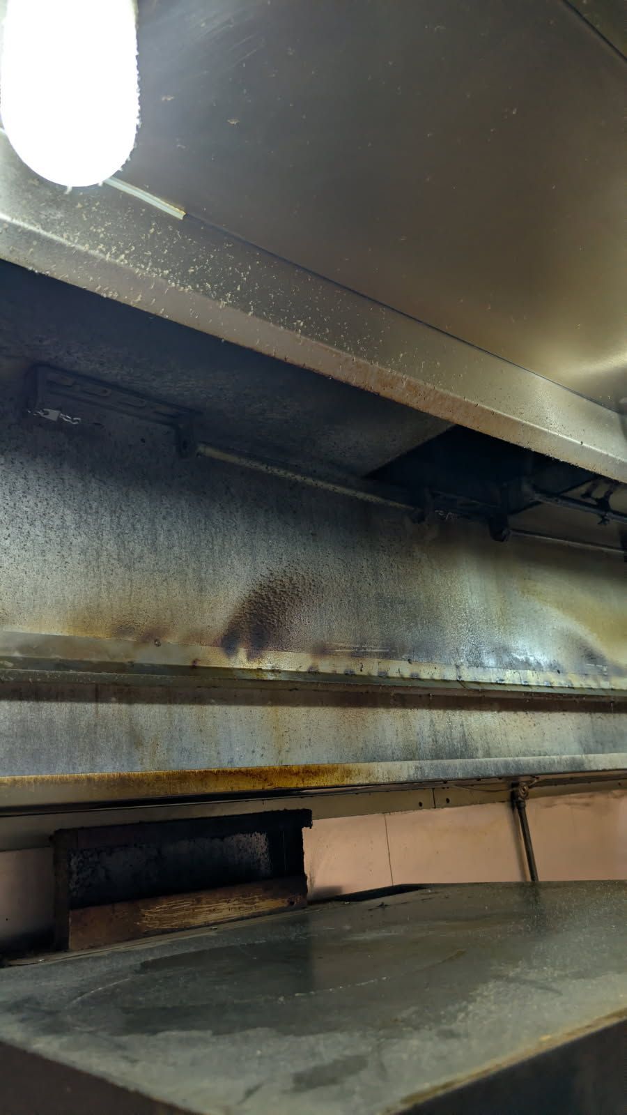 Interior of a commercial oven, showing the top, with dark stains and a light overhead.