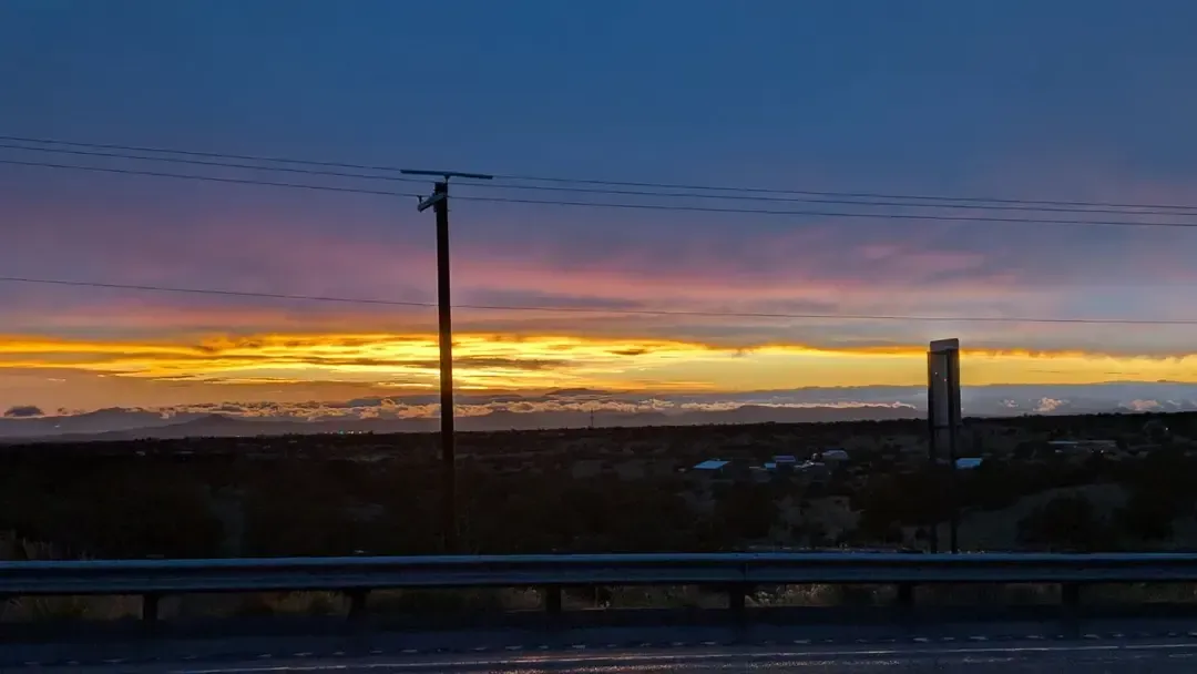 Sunset over a rural landscape, with a utility pole in the foreground and colorful sky gradients of blue, orange, and pink.