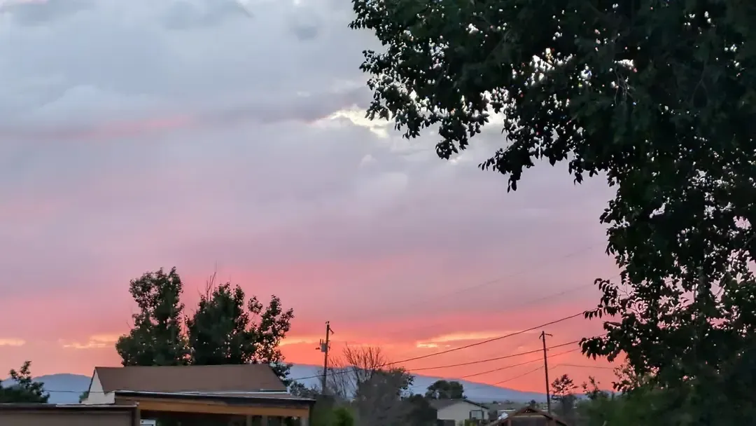 Vibrant pink and orange sunset over a landscape, with silhouetted trees and a building.