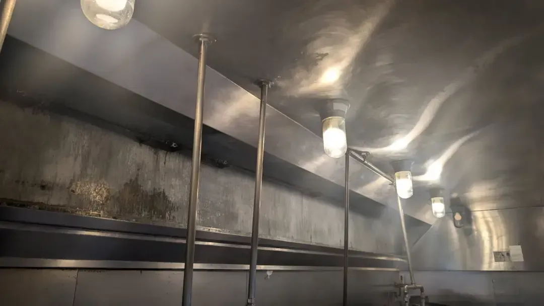 Stainless steel kitchen hood interior with lights and exhaust system. Sooty, dirty areas are visible.