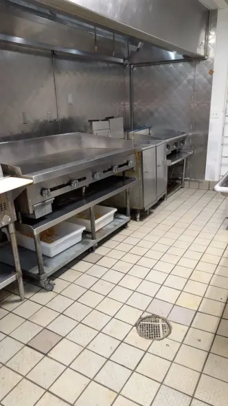 Stainless steel commercial kitchen with griddle and other cooking equipment. Tile floor.