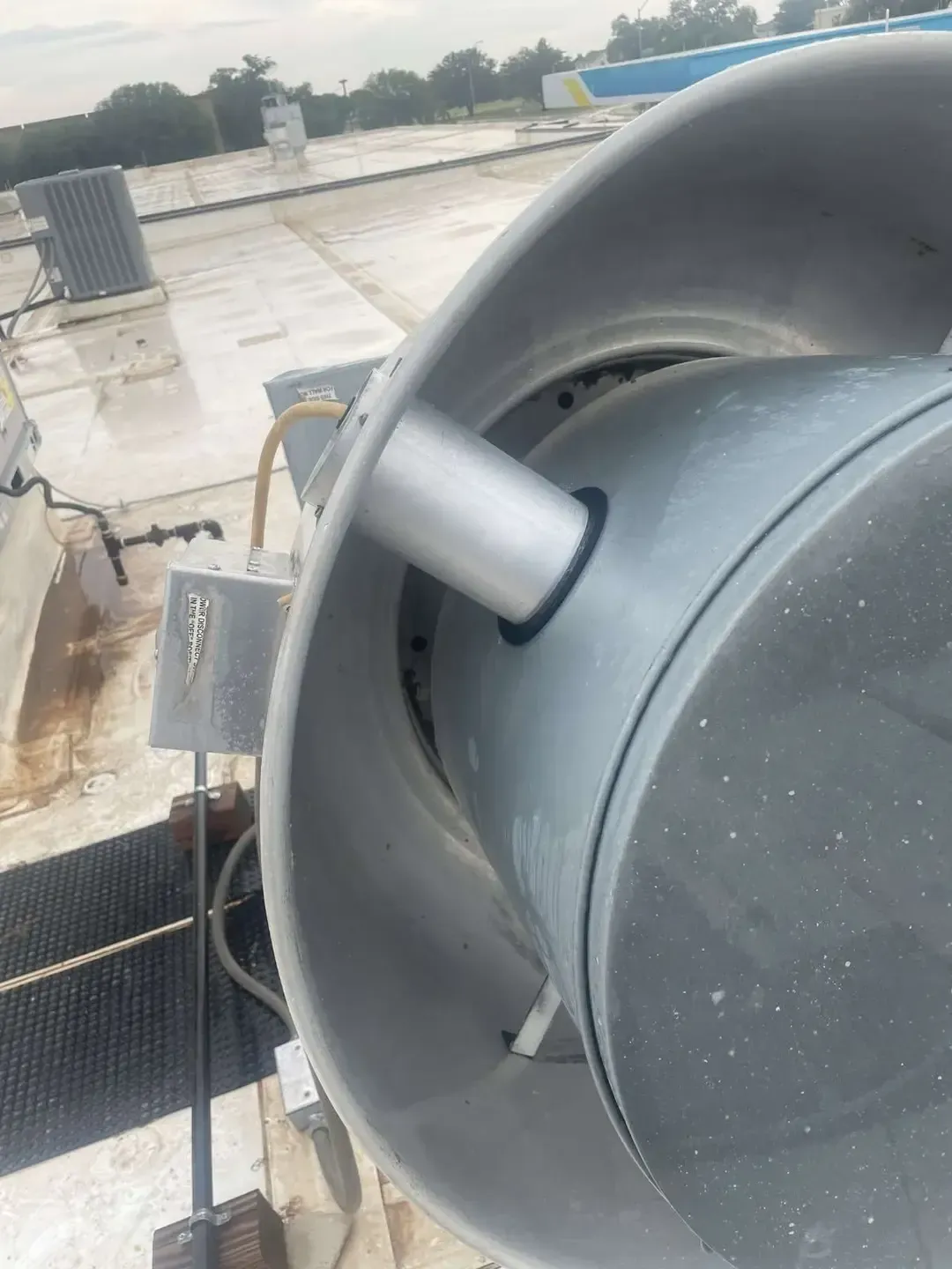 A large, cylindrical ventilation unit on a rooftop with a metal exterior and a small pipe attached to the side.