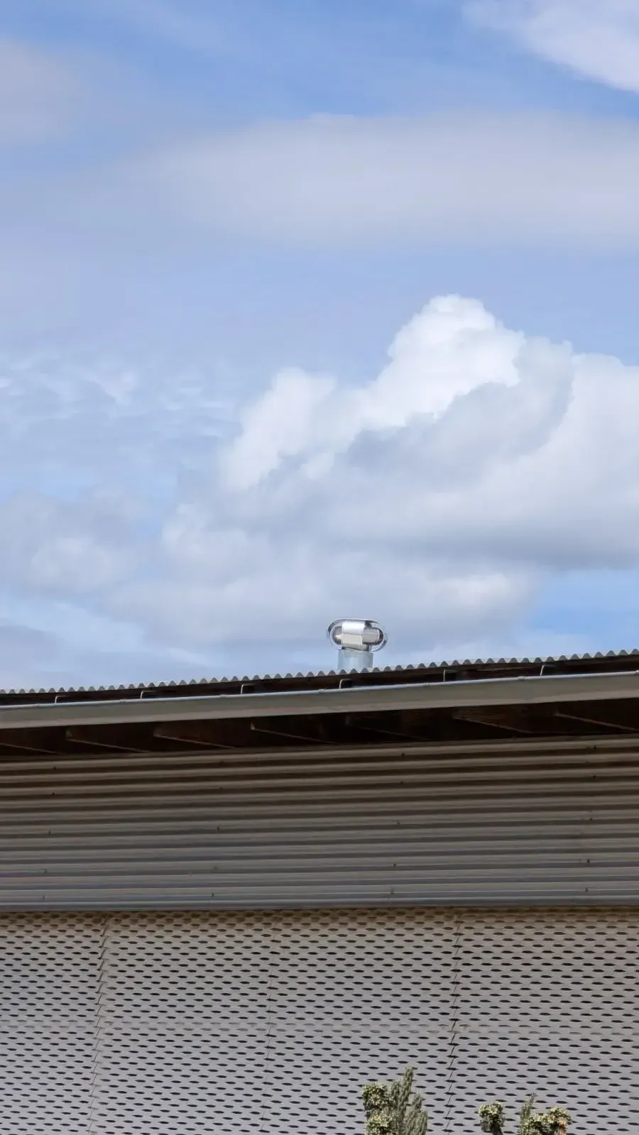 A silver vent cap on a corrugated metal roof against a partly cloudy blue sky.