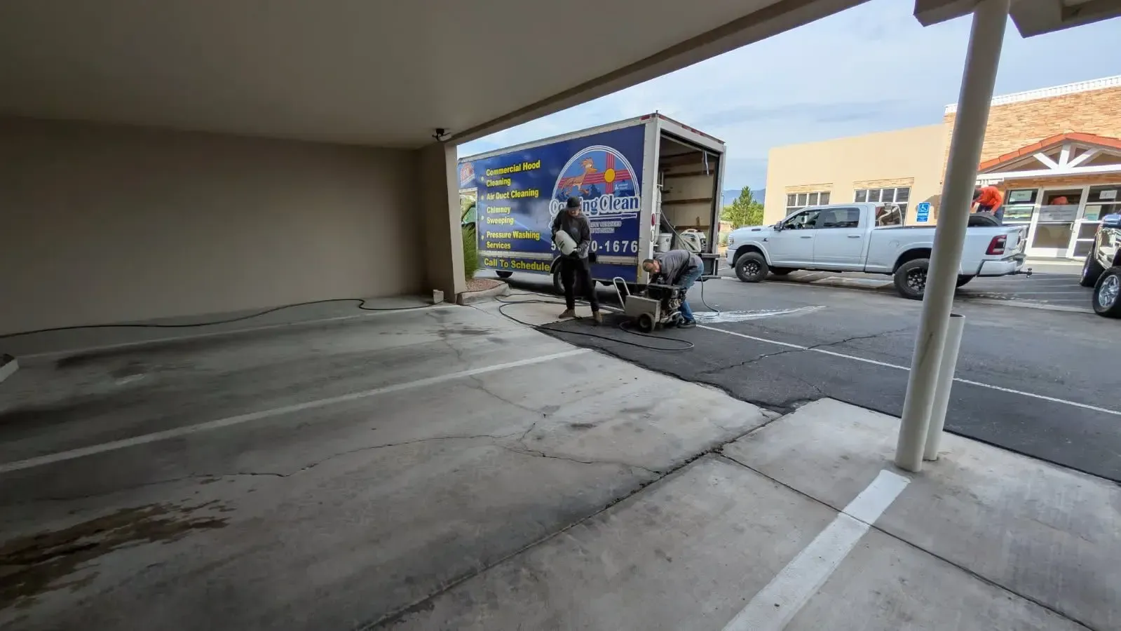 Two men working near a moving truck in a parking lot. One uses a saw, while another watches.