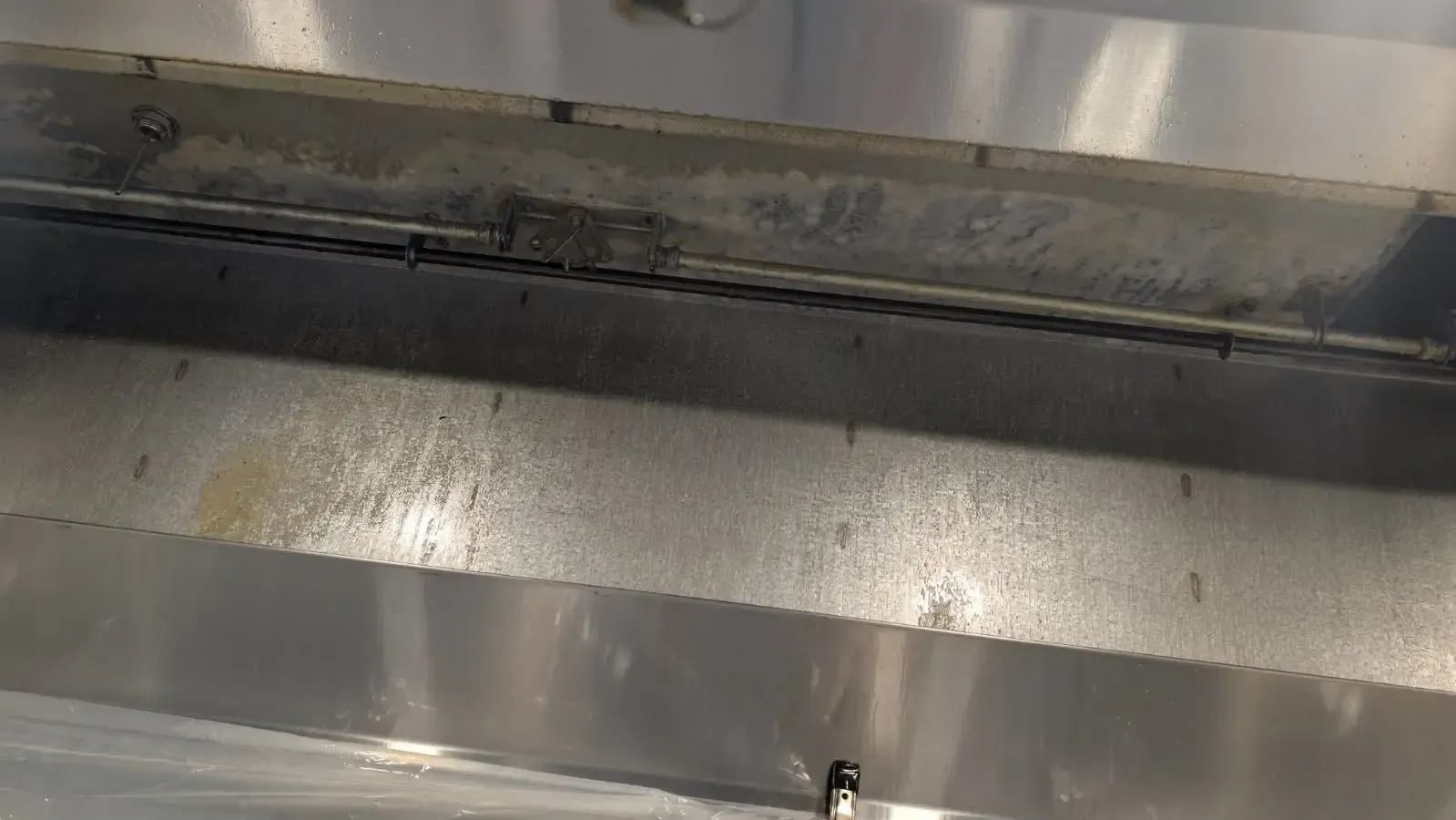 Inside view of a stainless steel commercial kitchen hood, showing dirty, stained surfaces and a wire mesh filter.