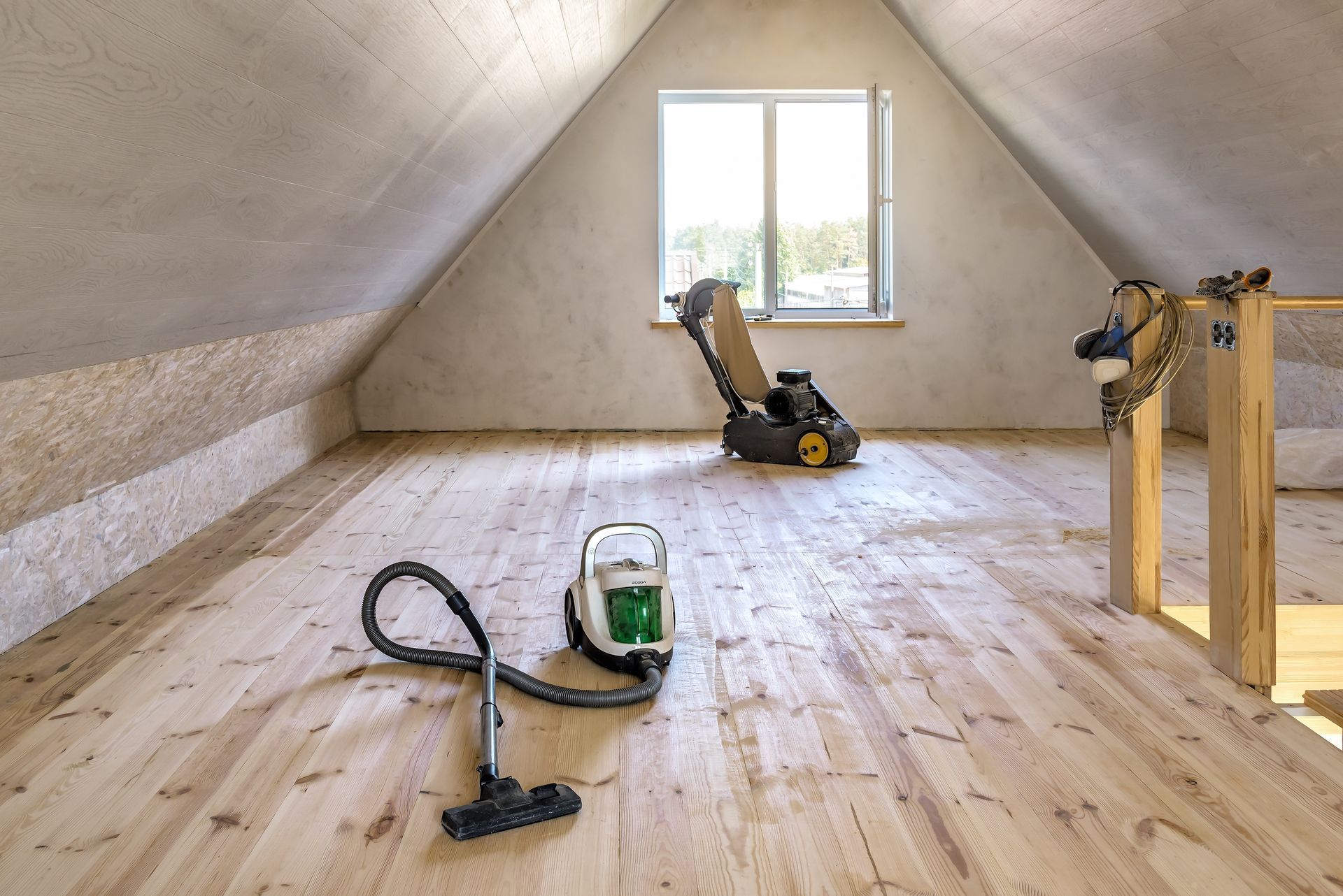 A vacuum cleaner is sitting on a wooden floor in an attic.