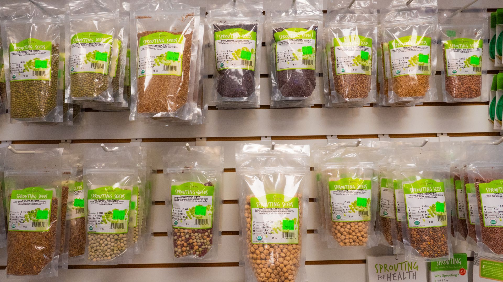 Shelves displaying sealed bags of various dried grains and beans in a store setting, each with a green label.