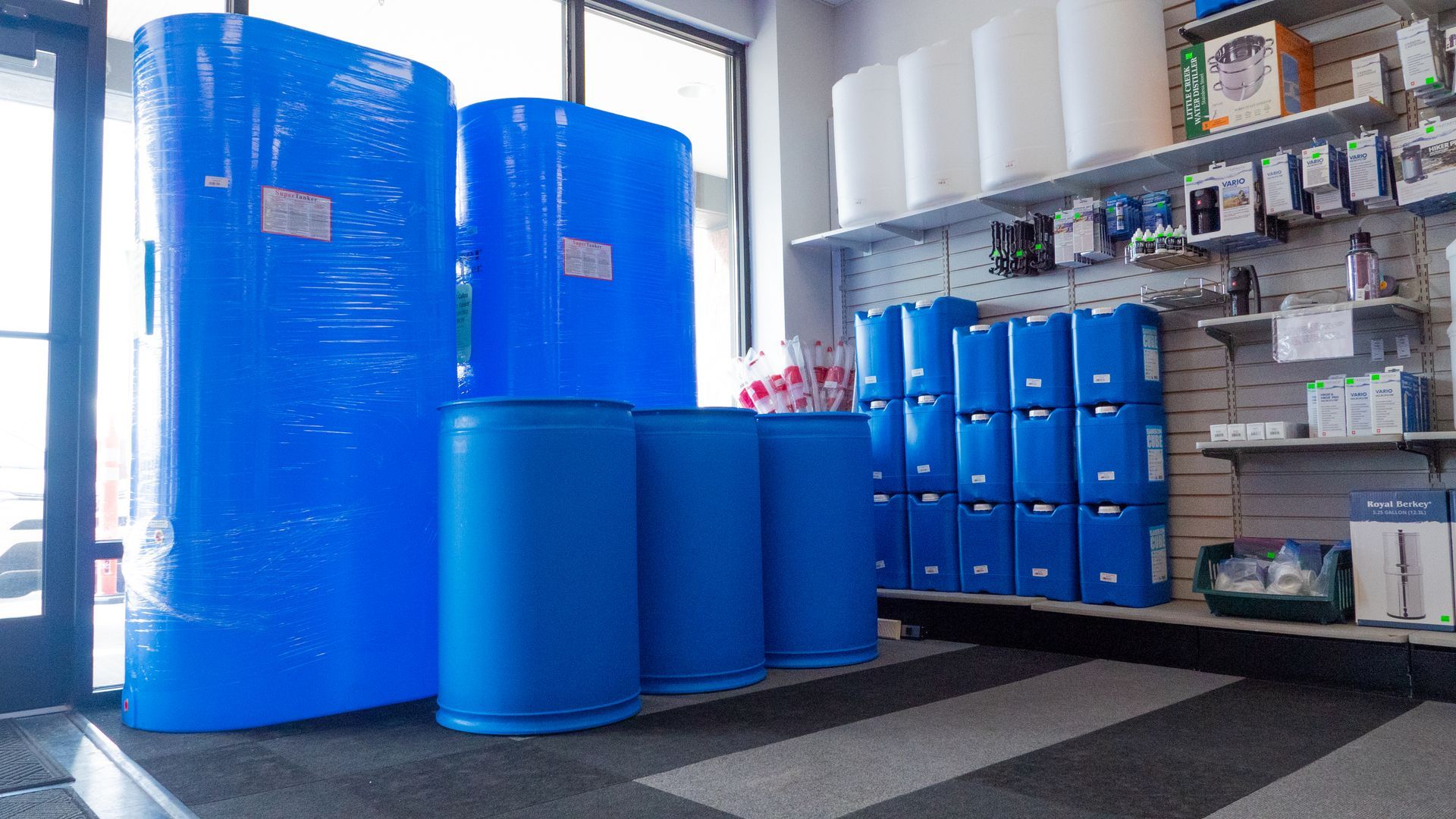 Blue water tanks and barrels are displayed inside a store with a shelf of white tanks and other products.