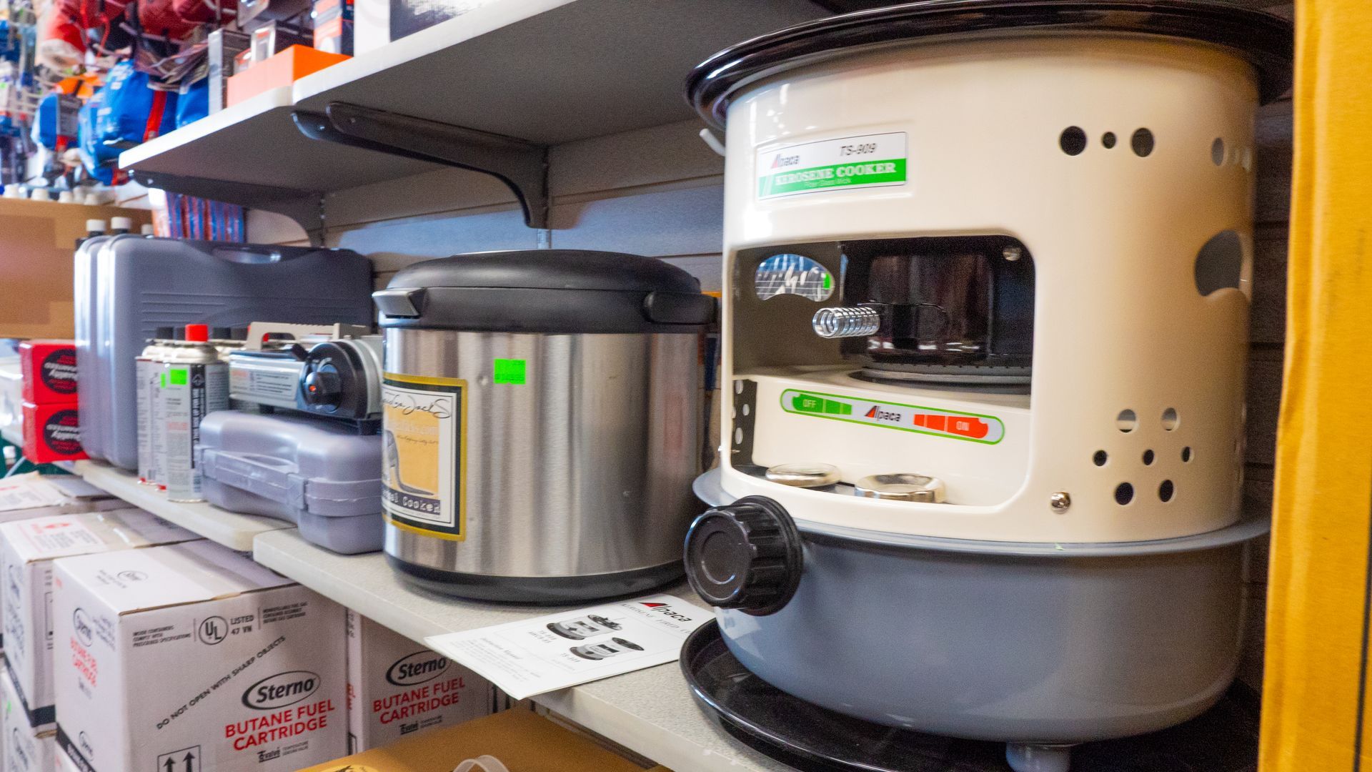 A shelf in a store displaying various appliances, including a kerosene heater and a rice cooker.