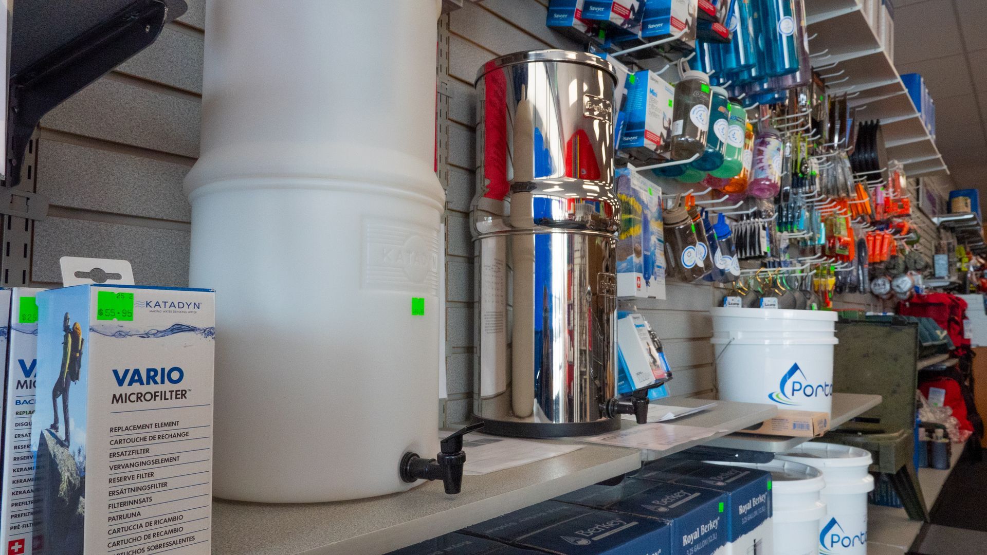 A store shelf displays water filtration systems, including a white plastic unit and a stainless steel model, along with accessories.