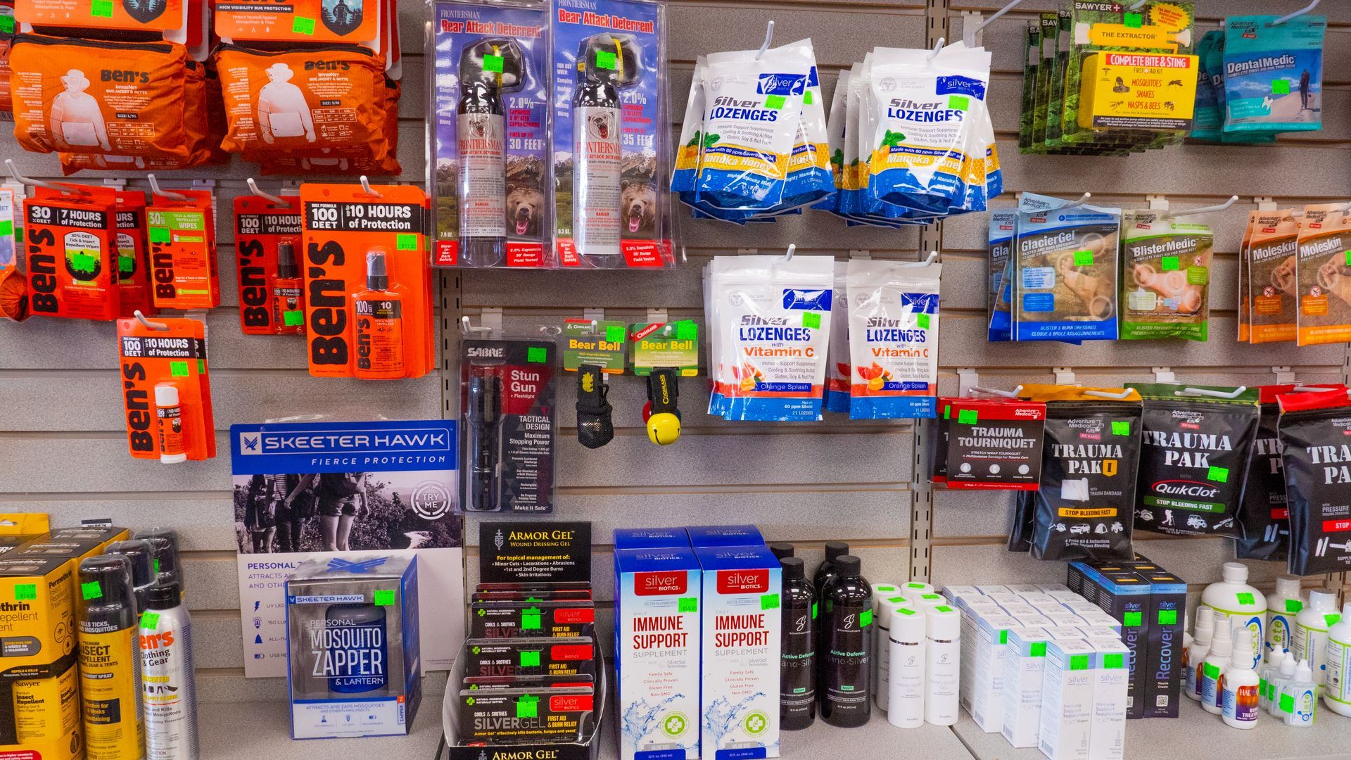 Shelves stocked with various camping and outdoor supplies in a store, featuring insect repellent, first aid kits, and food items.