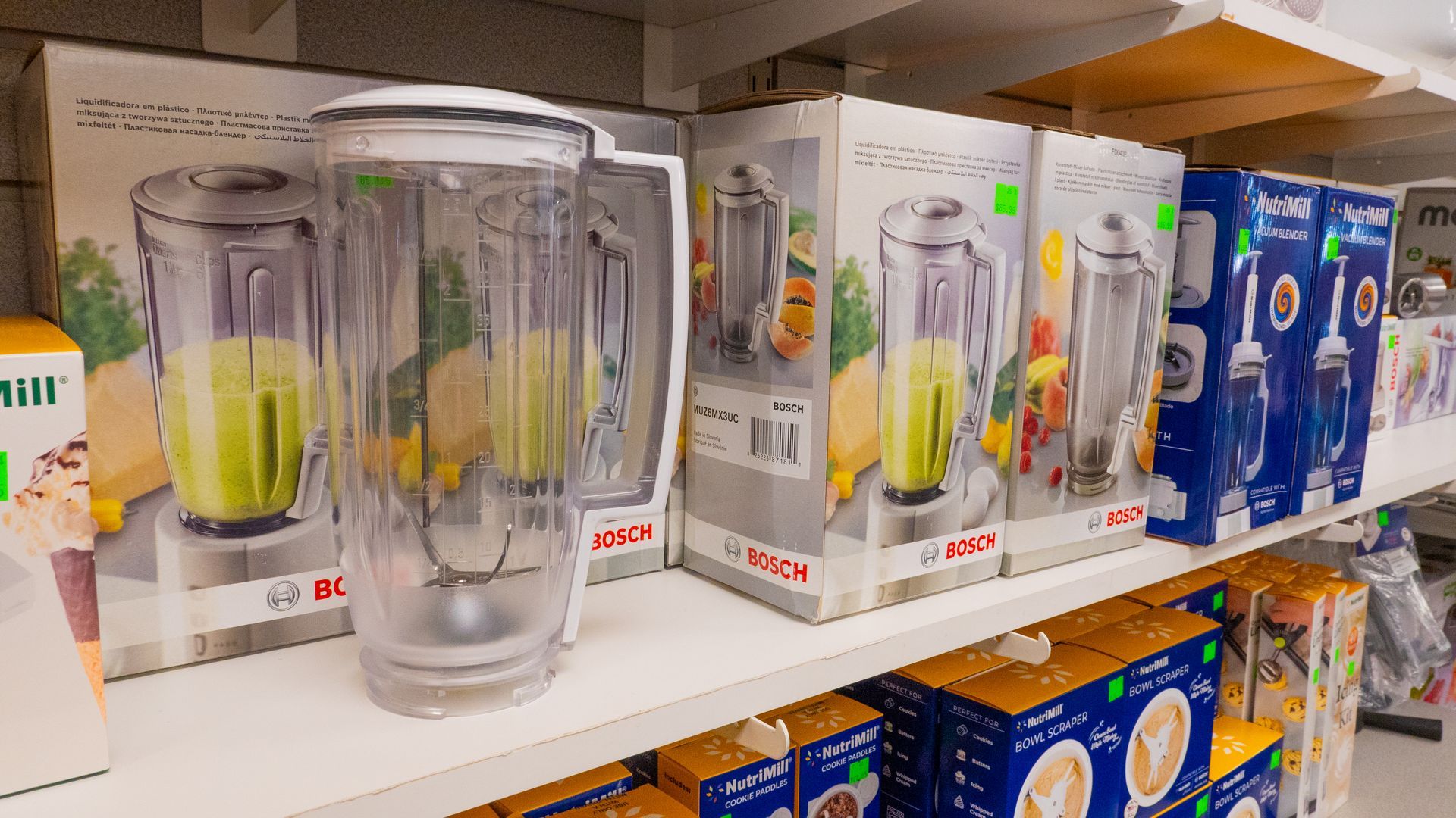Blenders on a store shelf in their boxes, featuring clear plastic pitchers. The boxes have images of the blenders and fruit.