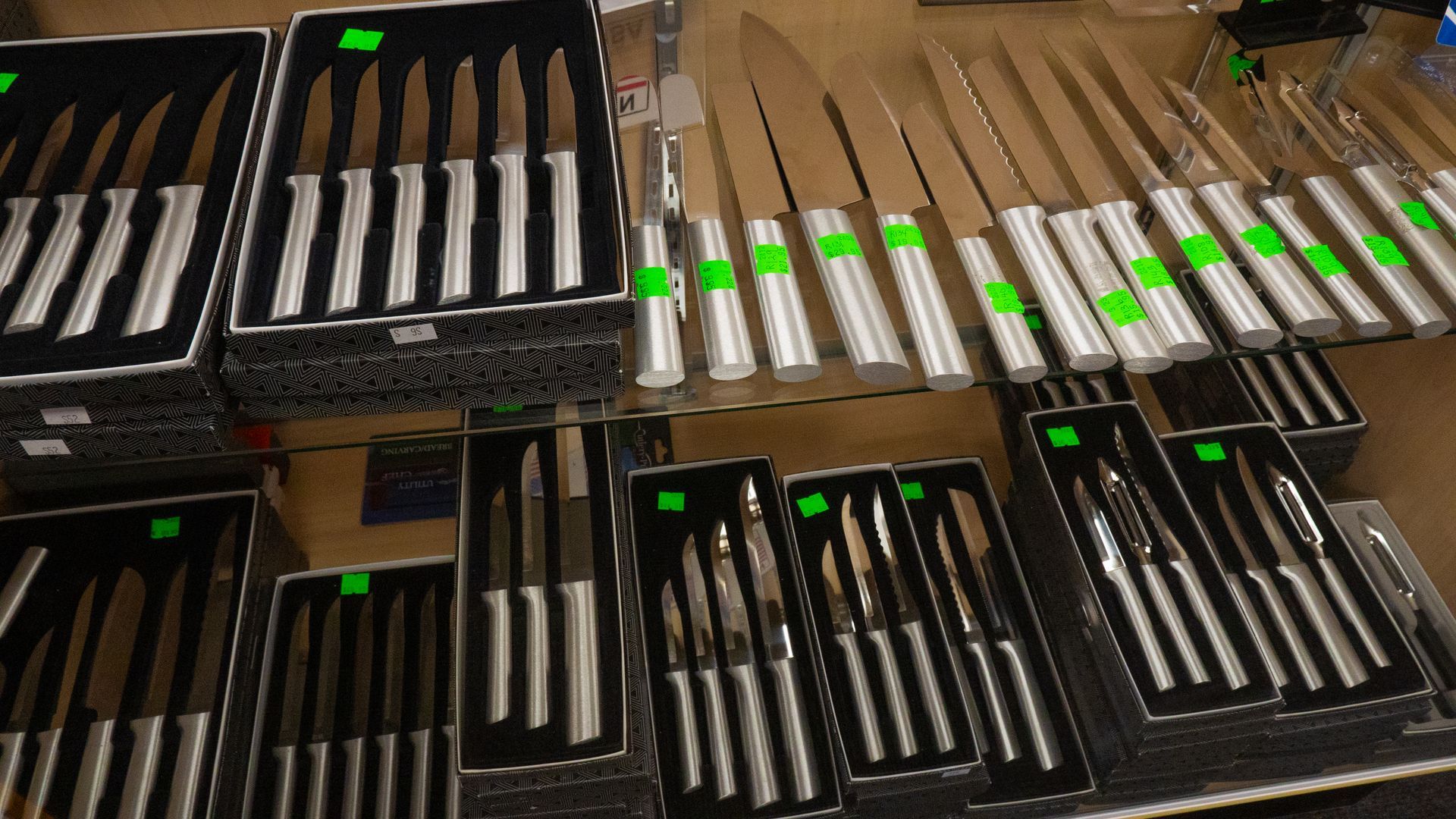 Display case filled with various sets of stainless steel knives, some with green price tags.